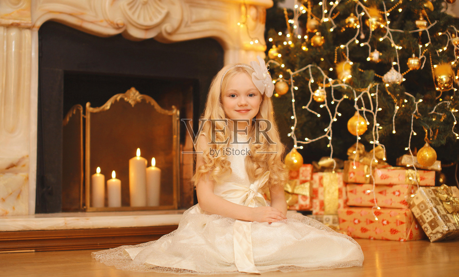 快乐的小女孩抱着节日的礼物盒，坐在家里的圣诞树和壁炉旁，脸上带着笑容照片摄影图片