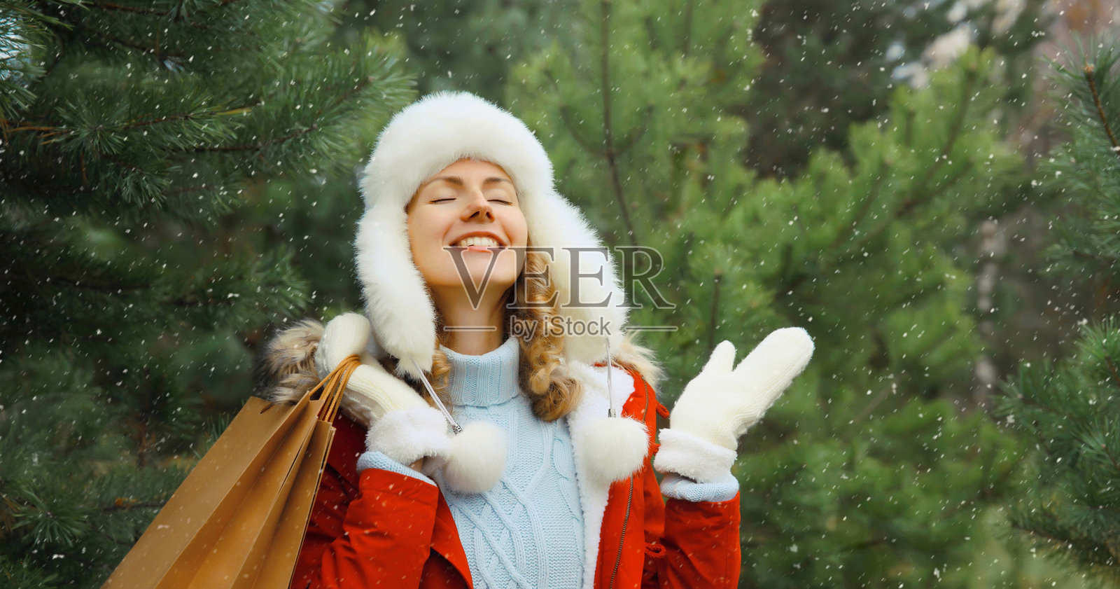 冬天里，一位快乐微笑的年轻女子提着购物袋，背景是圣诞树、雪景和节日购物。照片摄影图片