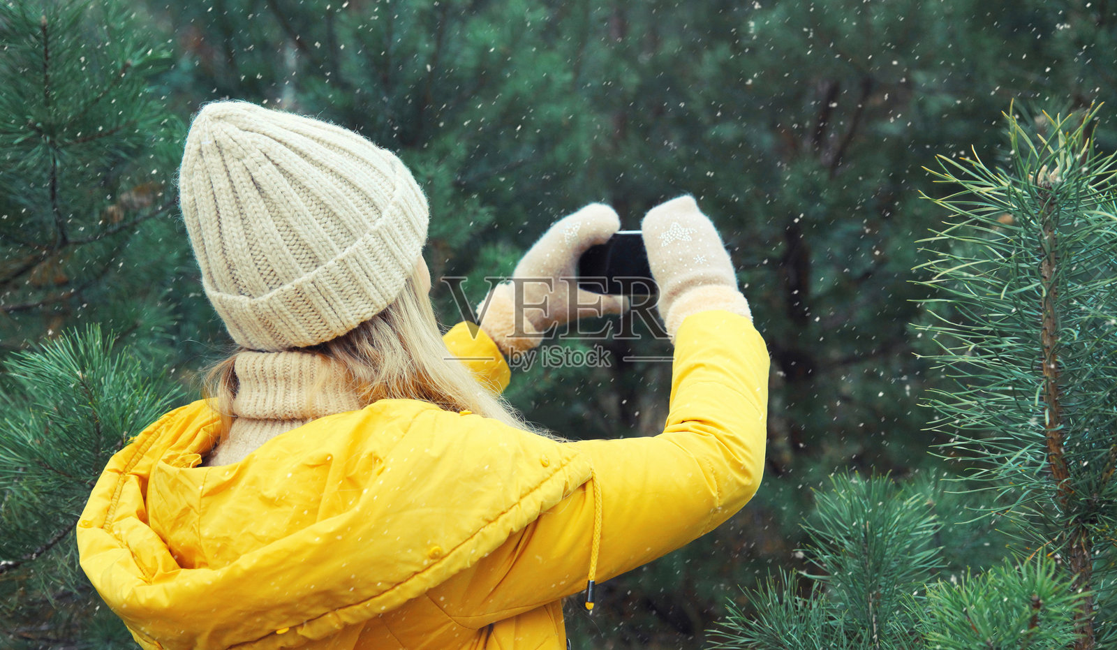 年轻女子在冬季公园用手机拍照，女孩在森林里玩智能手机照片摄影图片