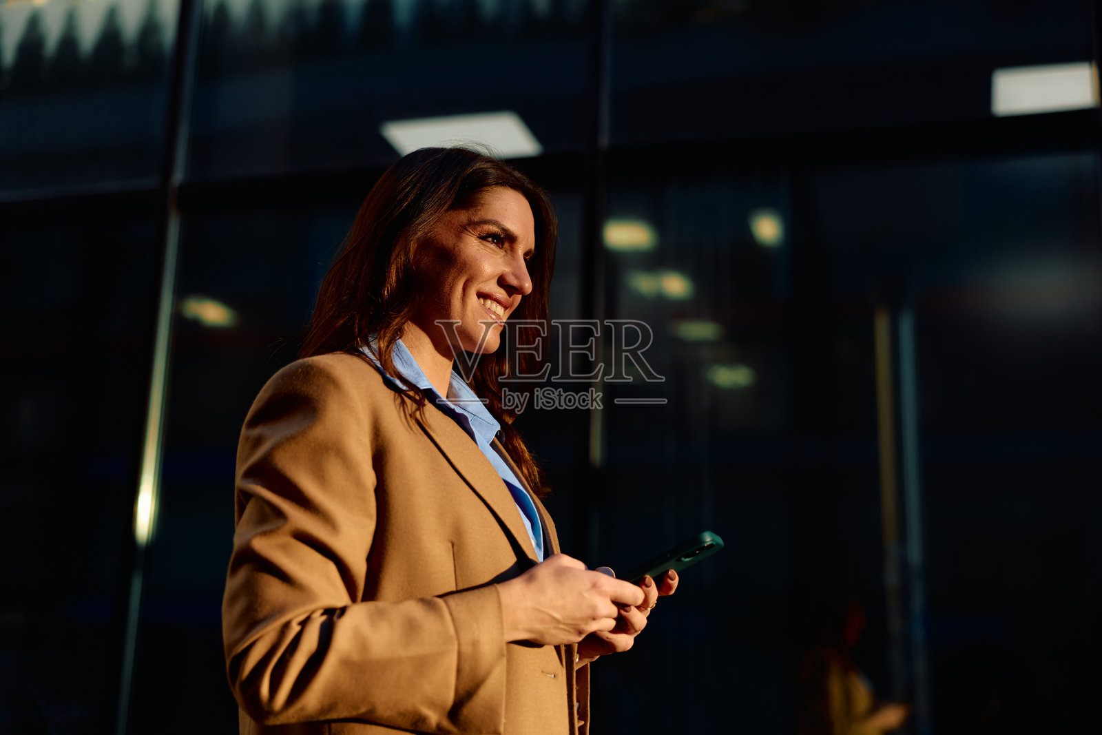 阳光下，一位女商人站在户外，面带微笑地使用智能手机。照片摄影图片