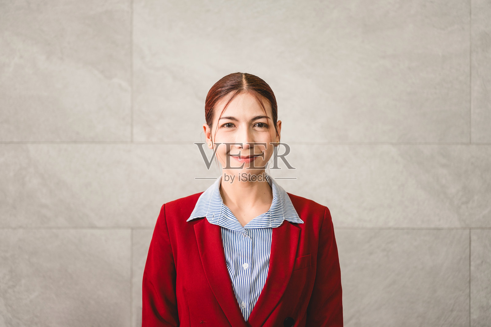 穿着红色西装外套的年轻专业人士，面带自信的笑容，站在浅色石墙前，现代商务着装，适合公司肖像，留有复制空间。照片摄影图片