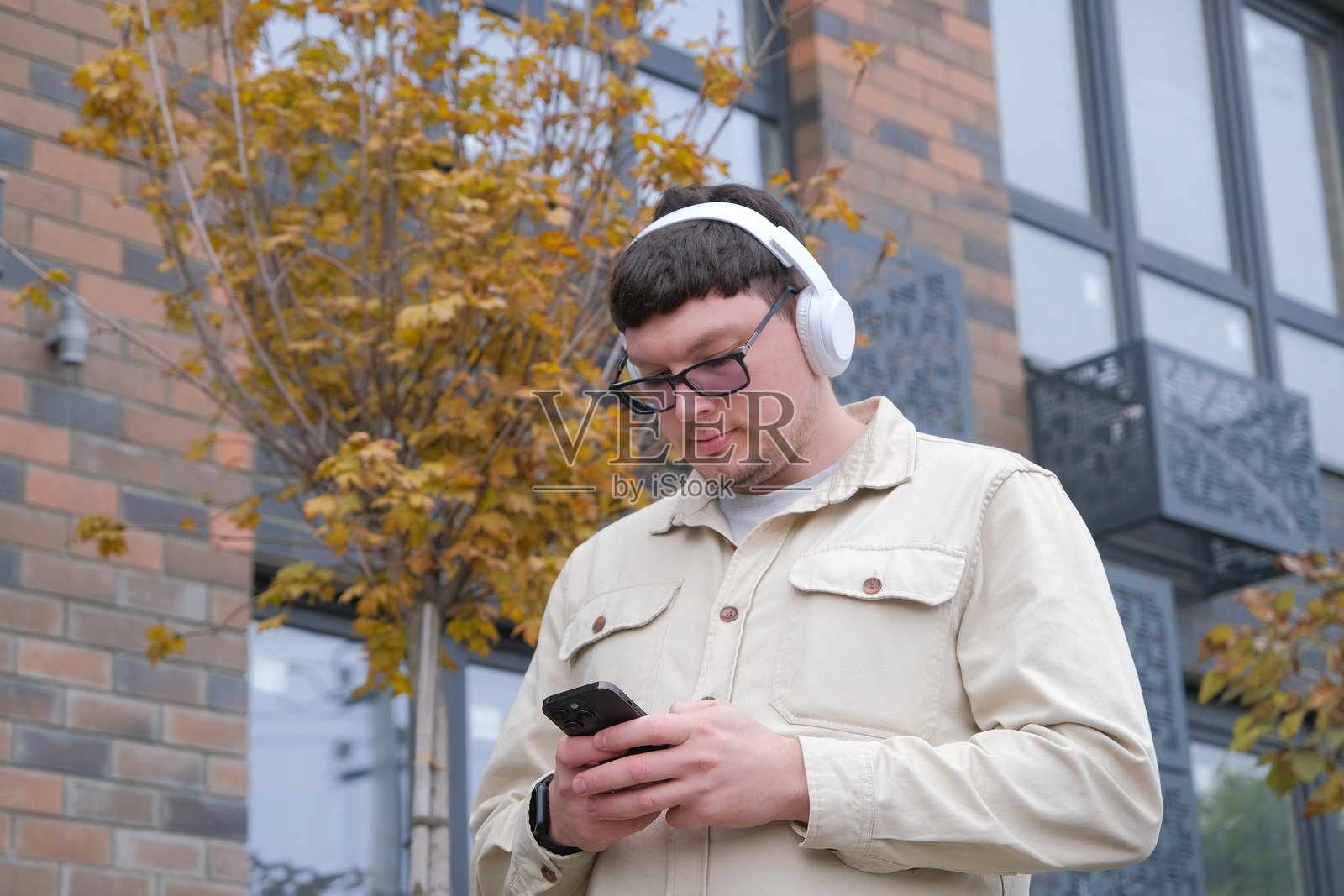 一个人戴着耳机，拿着智能手机，边走边听音乐，旁边是公寓楼。照片摄影图片