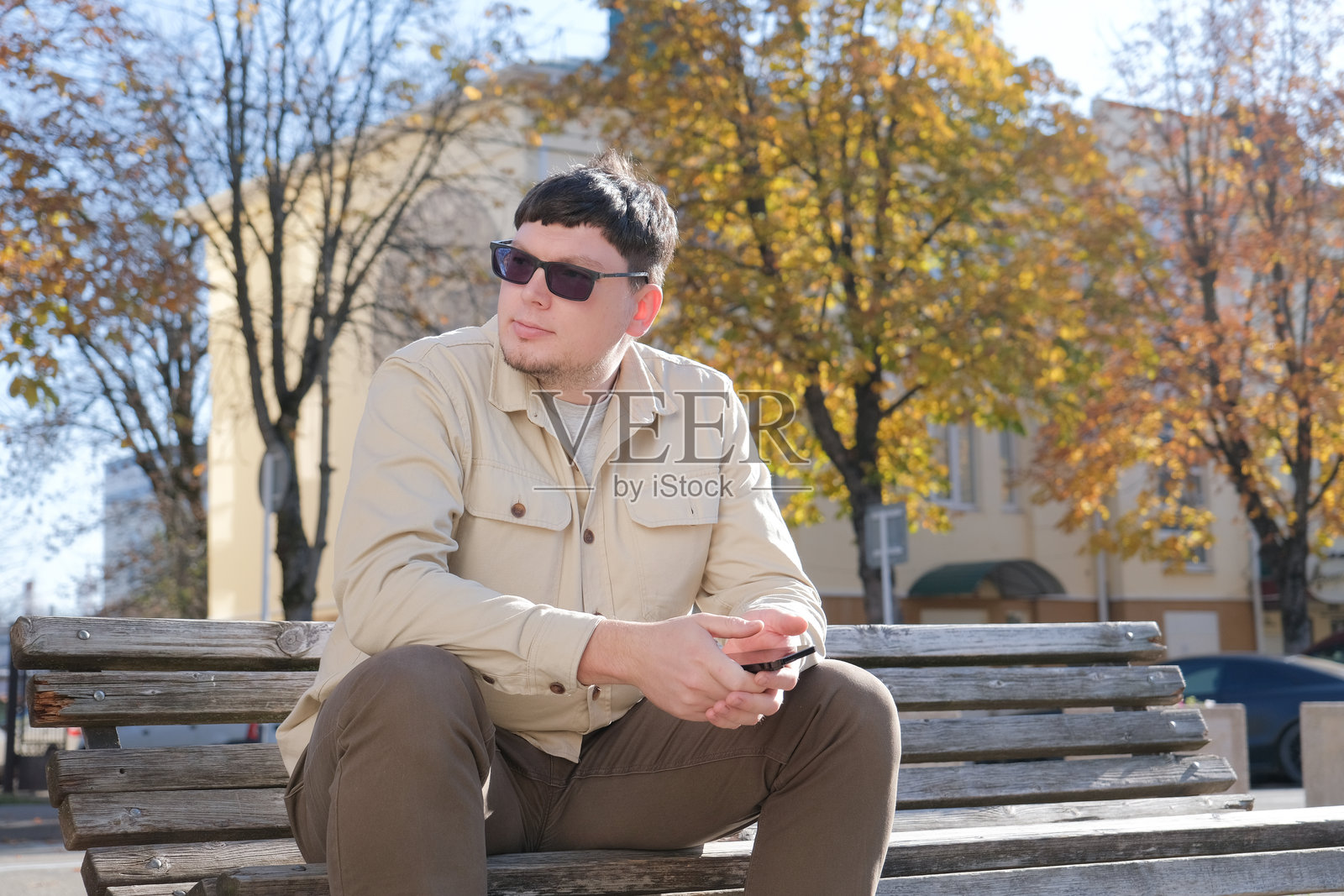 穿着休闲服的快乐男子坐在户外长椅上使用手机照片摄影图片