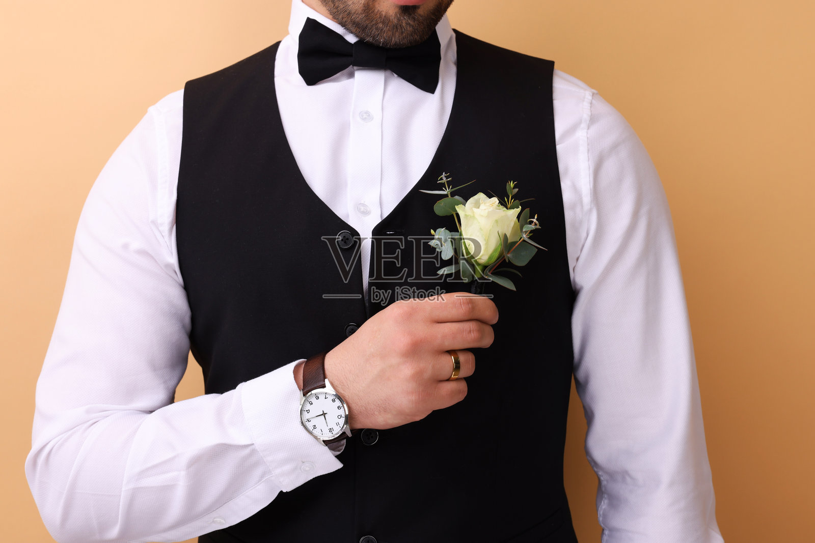 近景特写，新郎胸前佩戴襟花，背景为米色。婚礼配饰。照片摄影图片