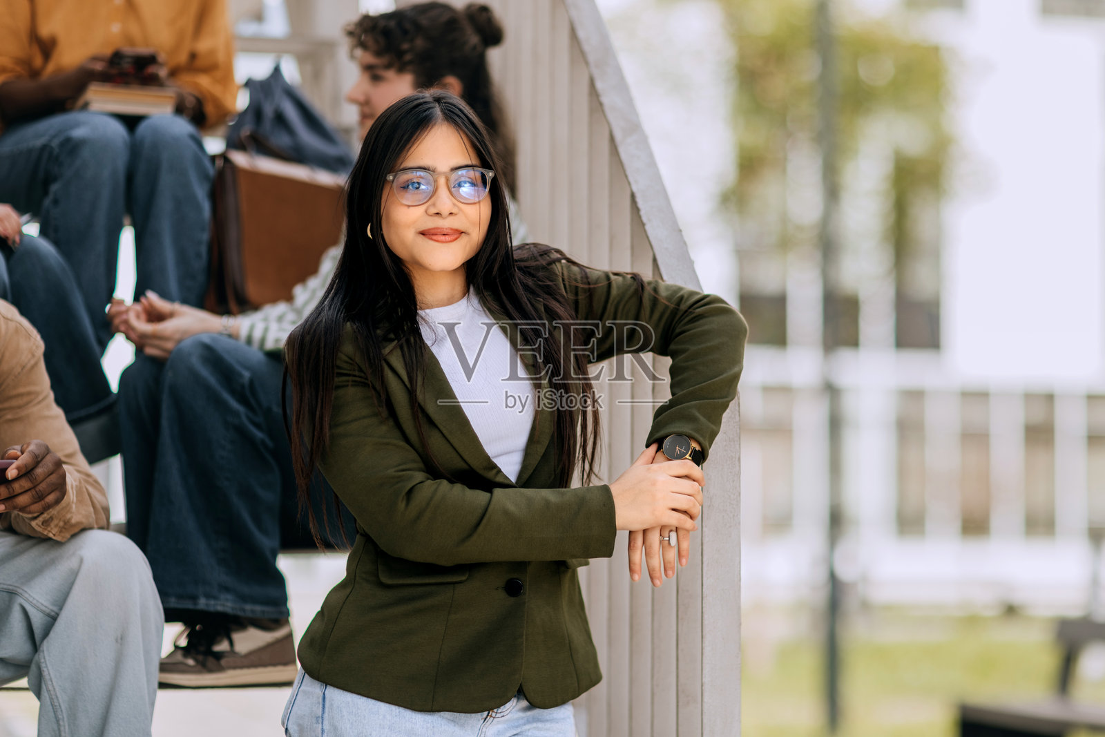 一位女学生对着镜头摆姿势，她身后有朋友坐在楼梯上照片摄影图片