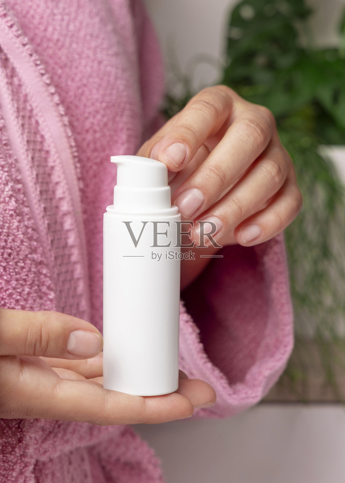 特写：女子身穿粉色浴袍，双手拿着白色乳霜瓶，化妆品模型照片摄影图片