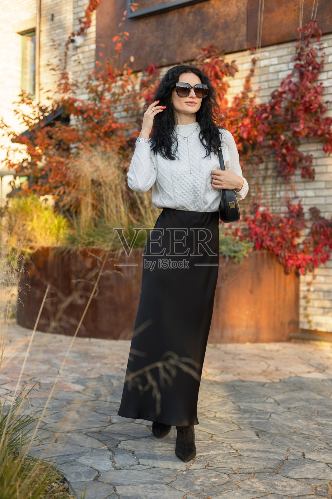 一位自信的女性身着别致的秋季服装，在爬满彩色常春藤叶子的乡村砖墙前摆姿势。照片摄影图片