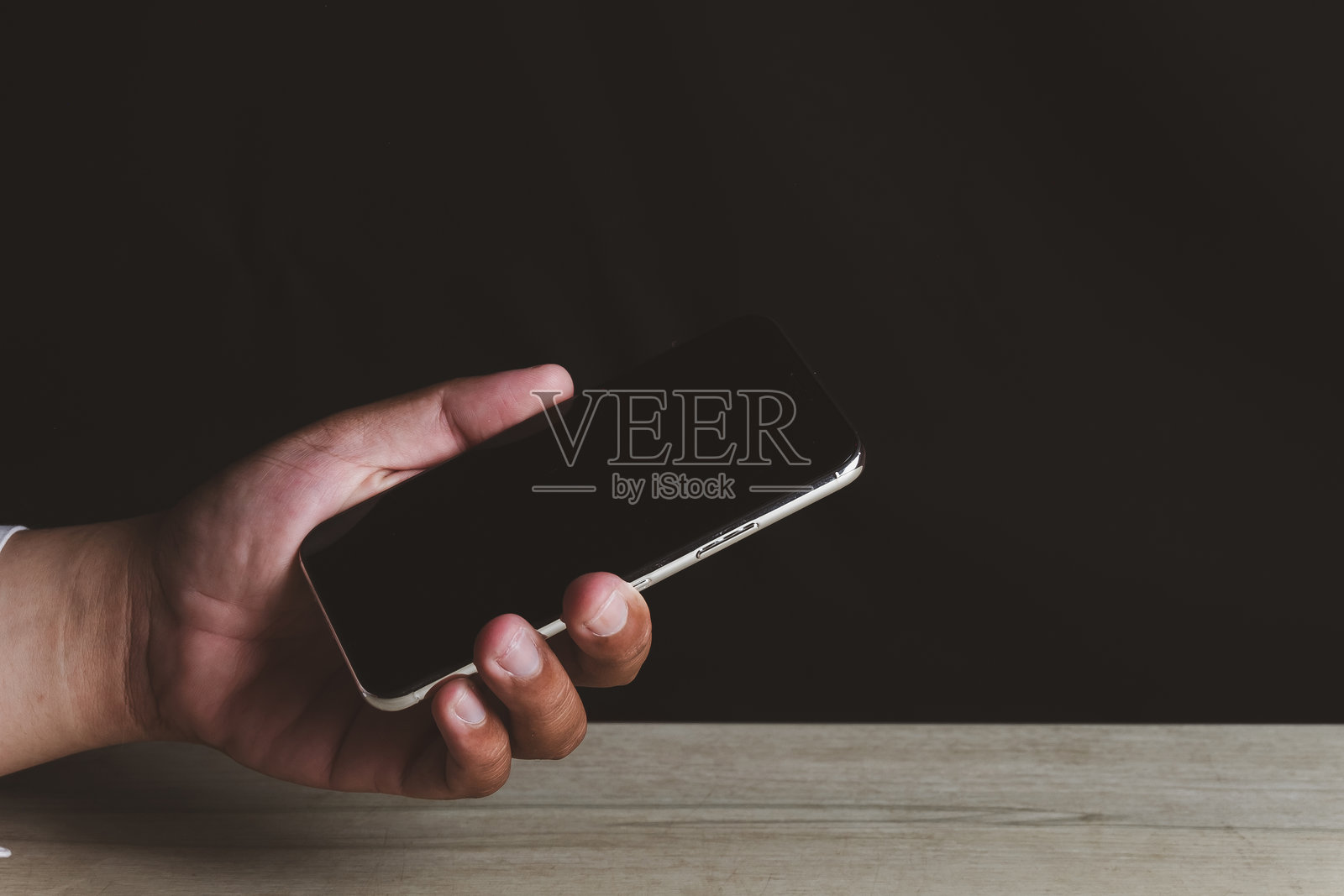 手持空白屏幕的智能手机：木制桌上的手机模型照片摄影图片