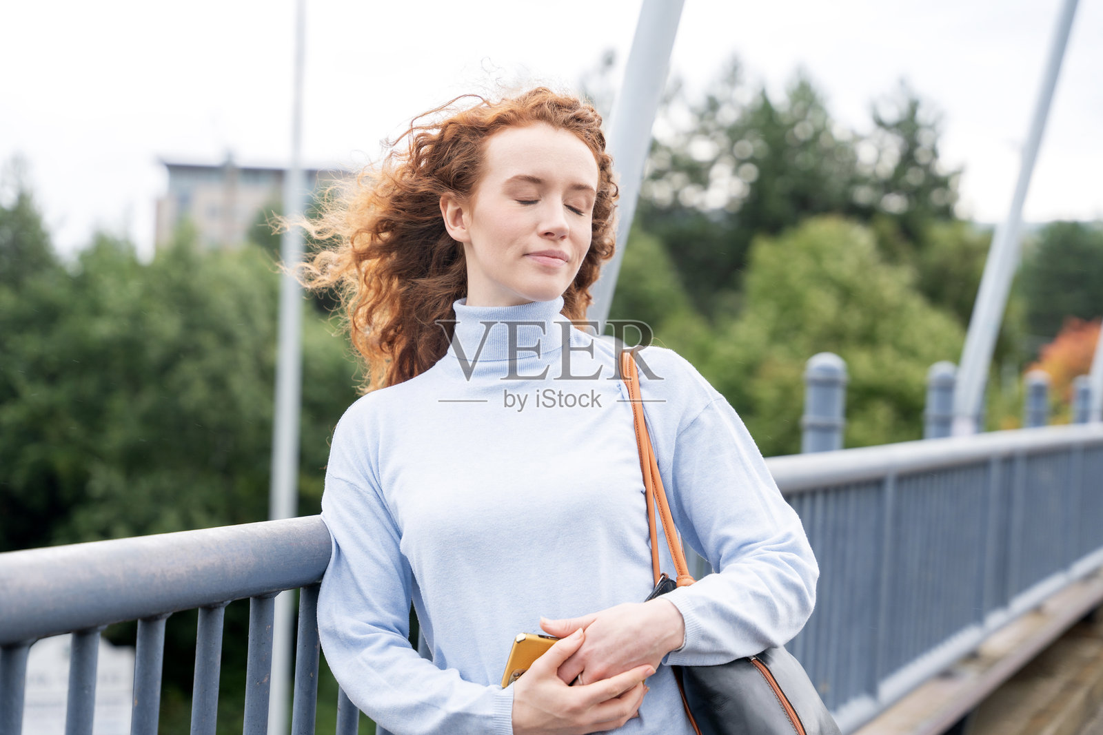 年轻女子在桥上放松，享受城市新鲜空气，手中拿着手机照片摄影图片