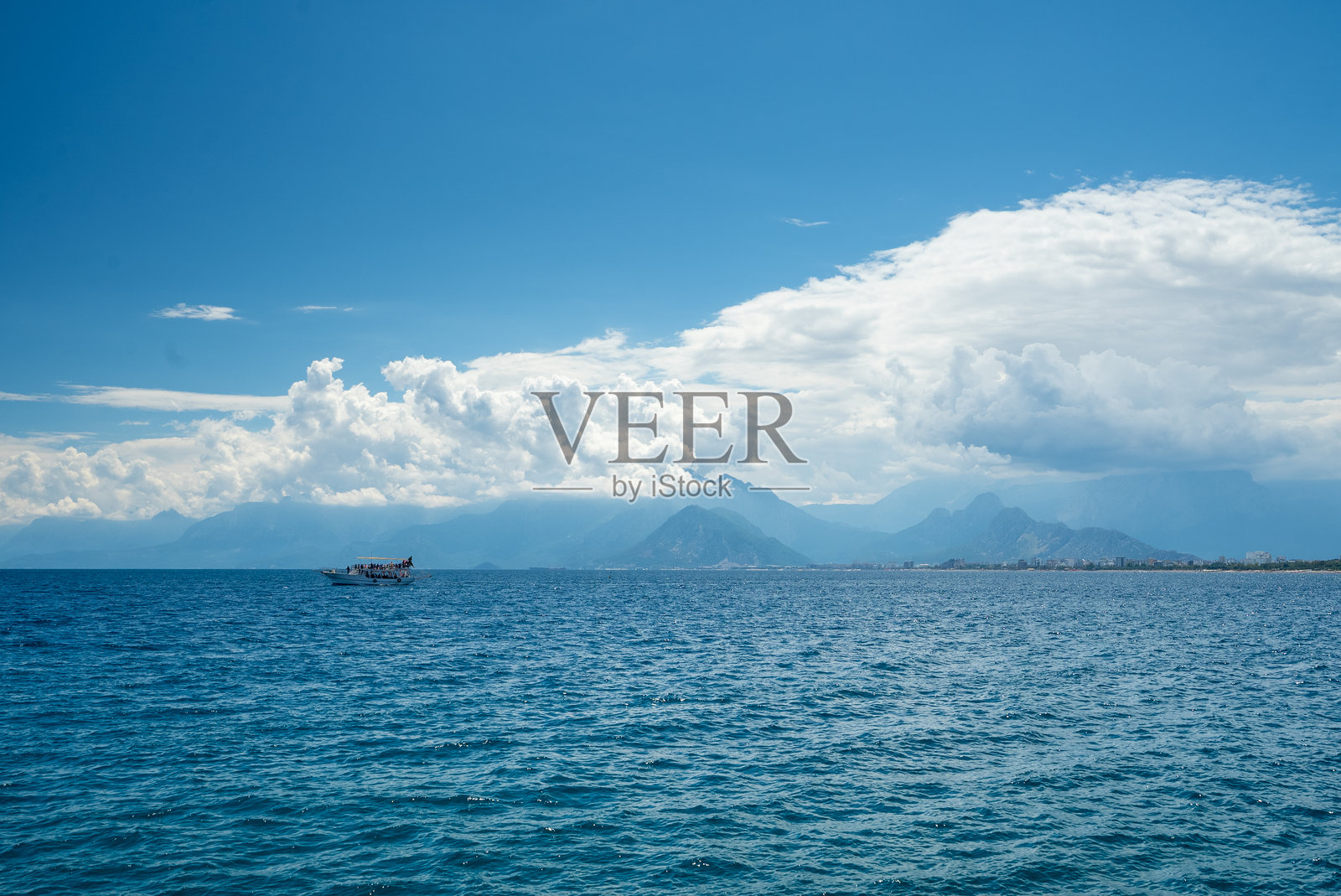 土耳其安塔利亚湾，地中海的蓝色海面上，风景如画的海景，一艘游船在多云的天空下，远眺壮丽的托罗斯山脉。照片摄影图片