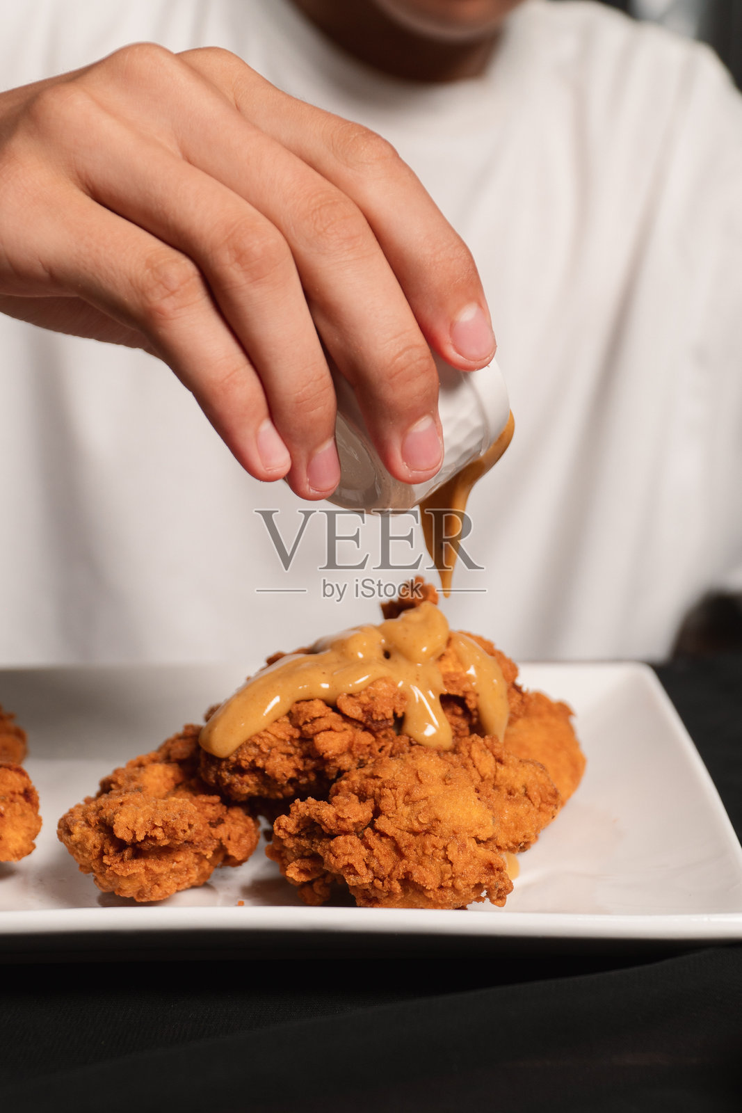 一只手将酱汁淋在装在盘子里的炸鸡上。照片摄影图片