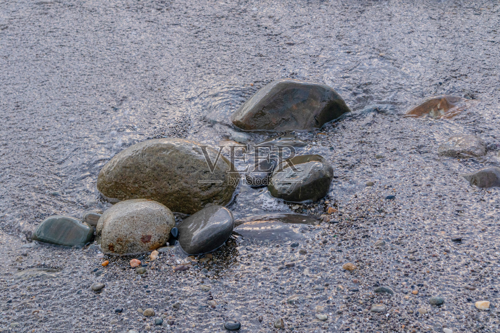 傍晚时分，光滑的大石头静静地躺在海边，宁静的海浪拍打着礁石。傍晚海景照片摄影图片
