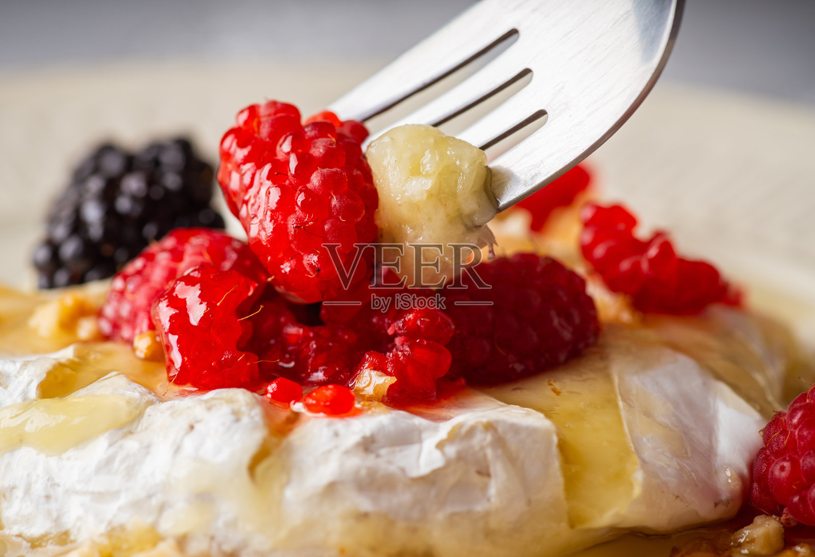 融化的卡门贝尔奶酪，上面点缀着覆盆子、黑莓、核桃和蜂蜜照片摄影图片