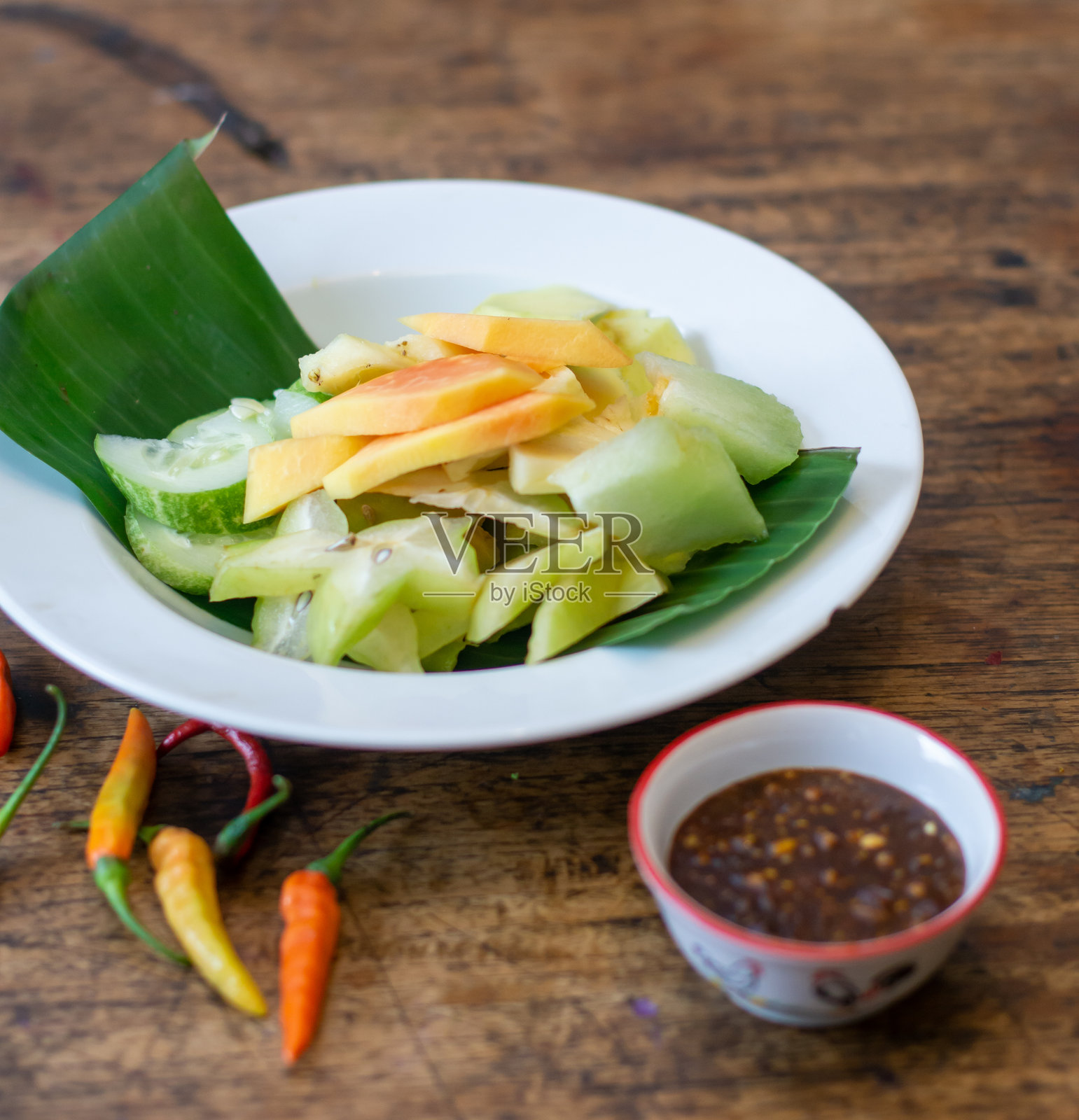 传统的印尼水果沙拉或 rujak serut，搭配辣味棕榈糖酱和辣椒，摆放在质朴的木桌上。照片摄影图片