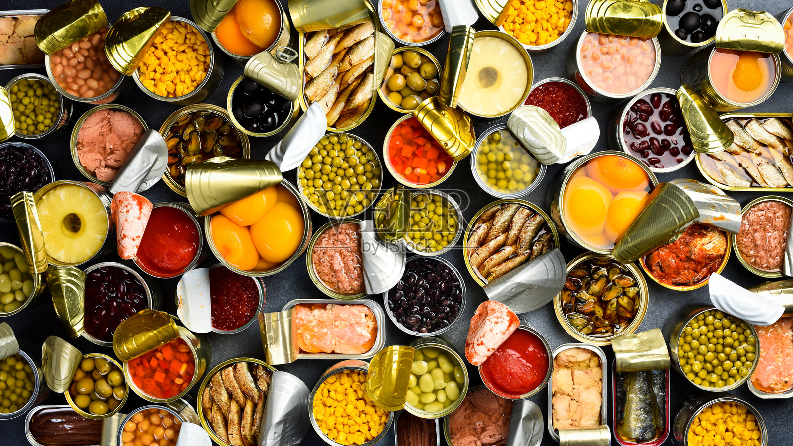 背景中大量的腌制和罐头食品。装有蔬菜、豆类、鱼类、海鲜和水果的金属罐头。俯视视角。照片摄影图片