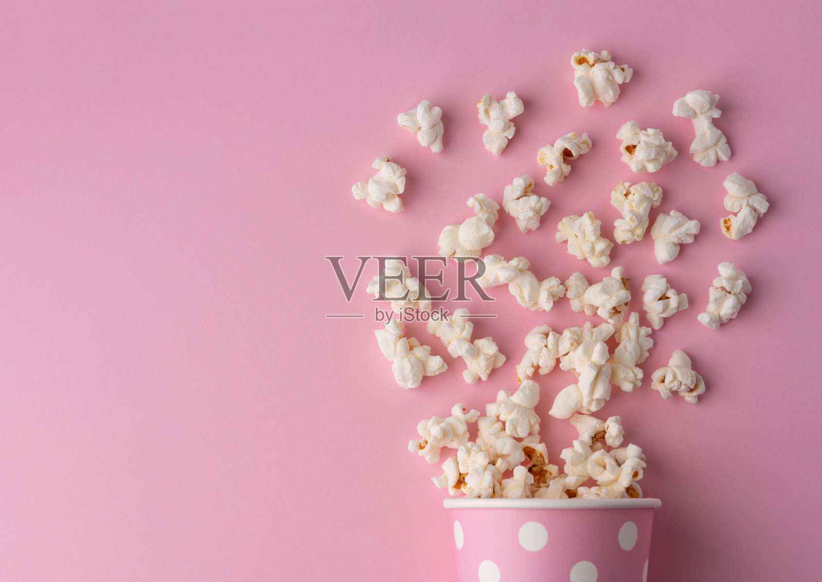 粉色背景上洒出的爆米花，电影、影片和娱乐概念照片摄影图片