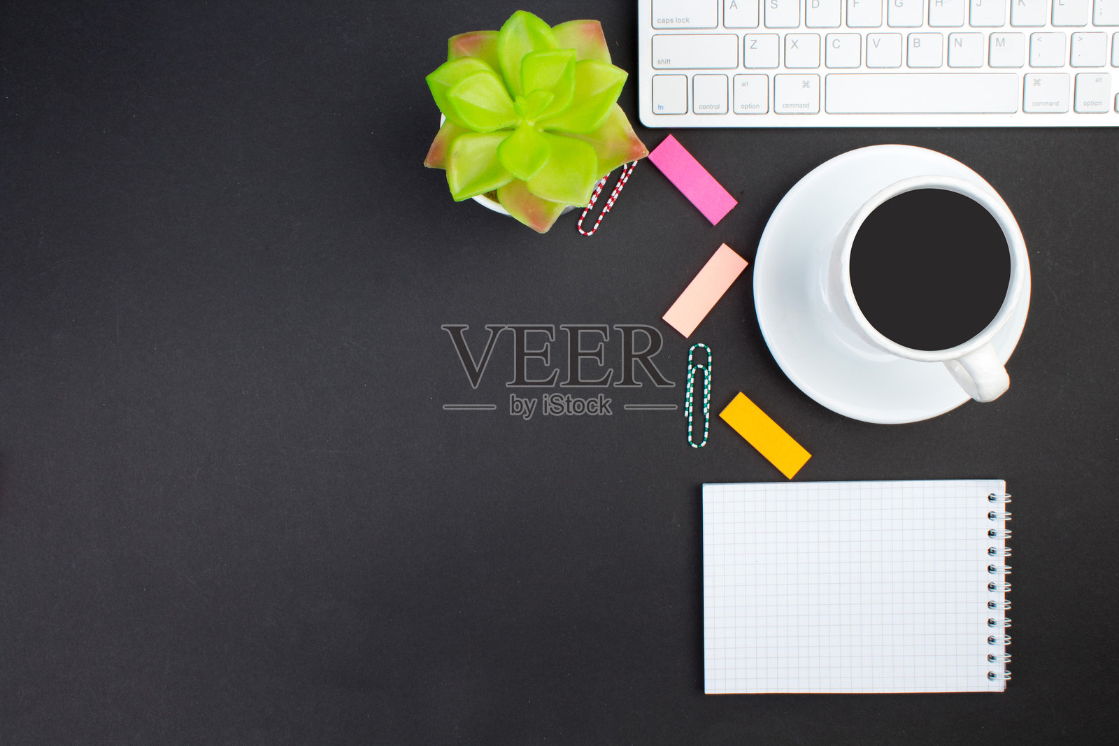 俯视角度的黑色办公桌，上面摆放着电脑、笔和咖啡杯，物品繁多，并留有复制空间。照片摄影图片