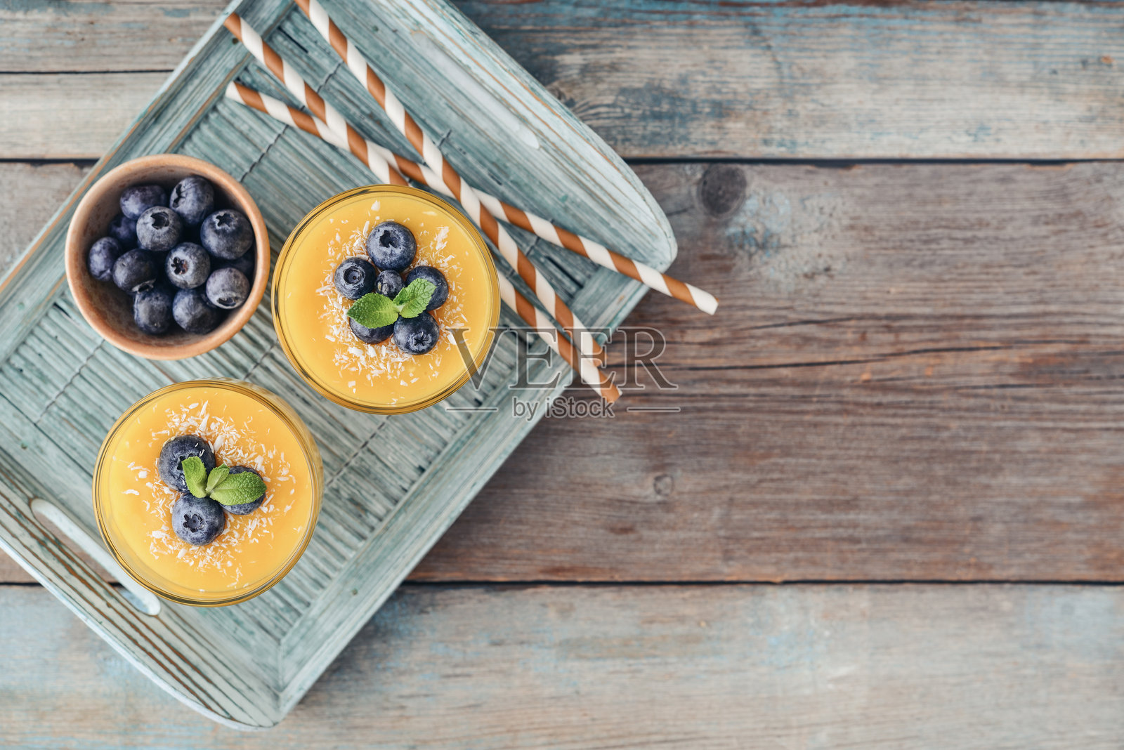 杯中盛着清爽健康的芒果冰沙，撒上椰子片并点缀新鲜蓝莓照片摄影图片