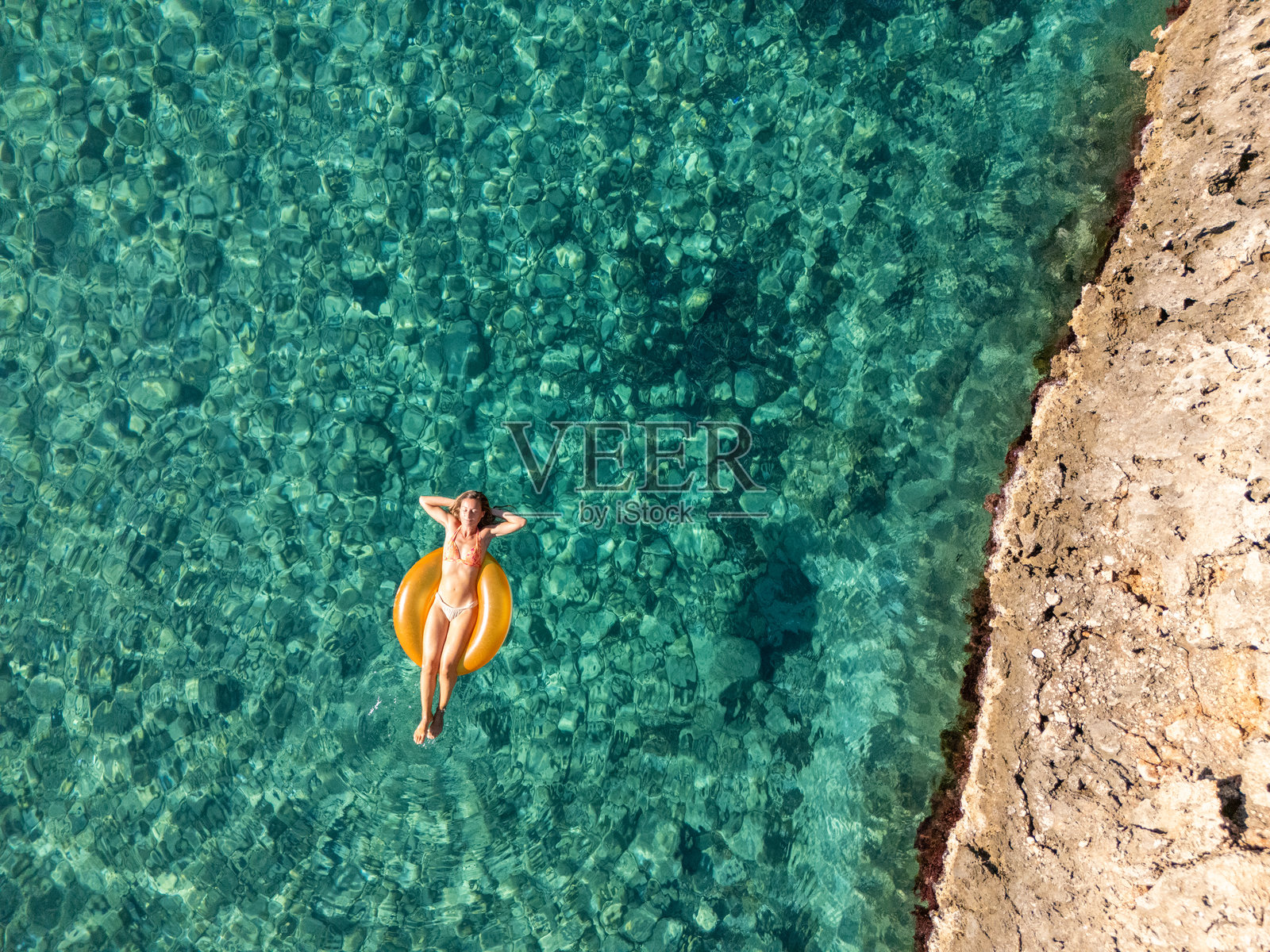 无人机视角拍摄：女子漂浮在清澈的蓝色水面上放松照片摄影图片