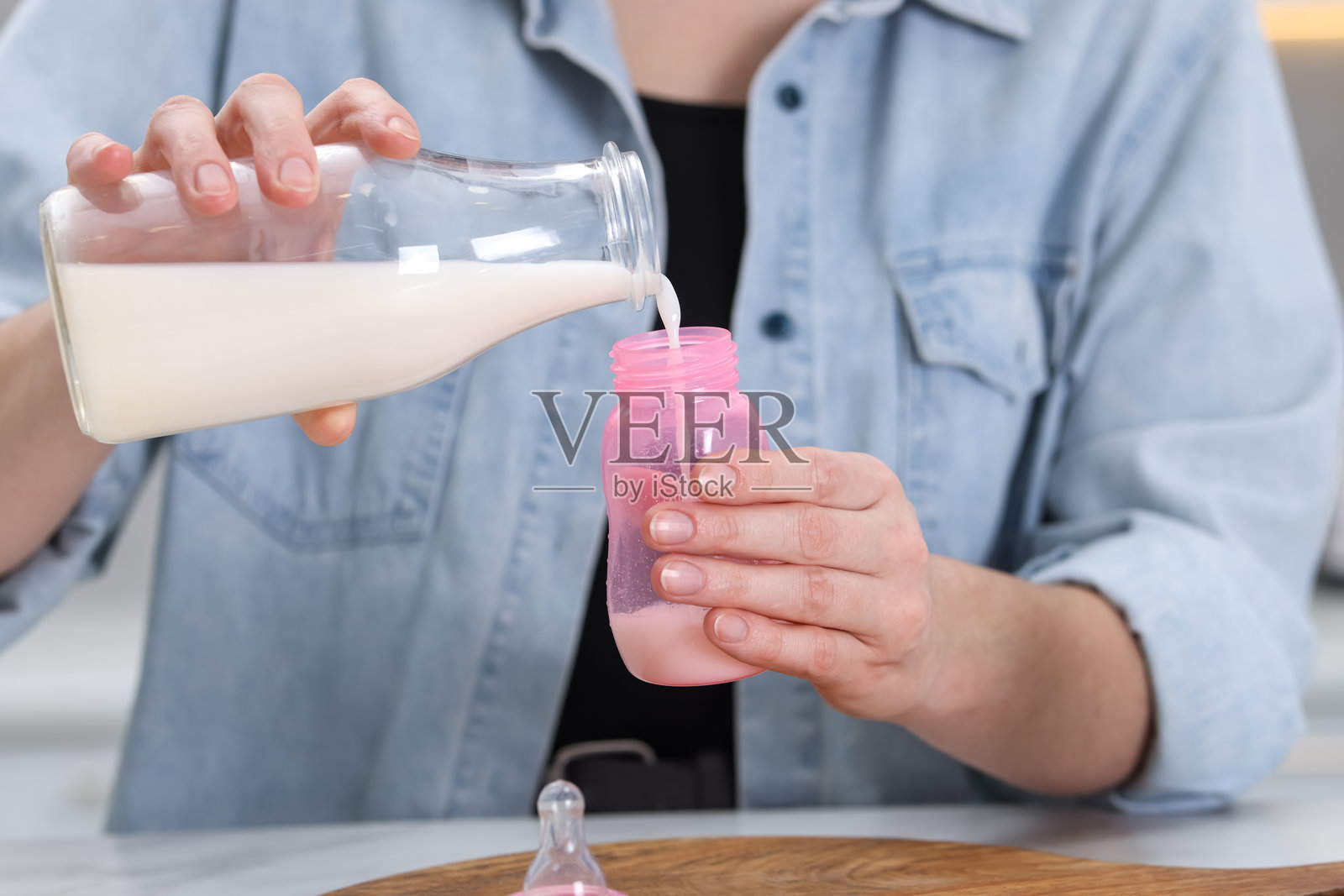 近距离特写：母亲在桌边用奶瓶为婴儿冲泡配方奶照片摄影图片