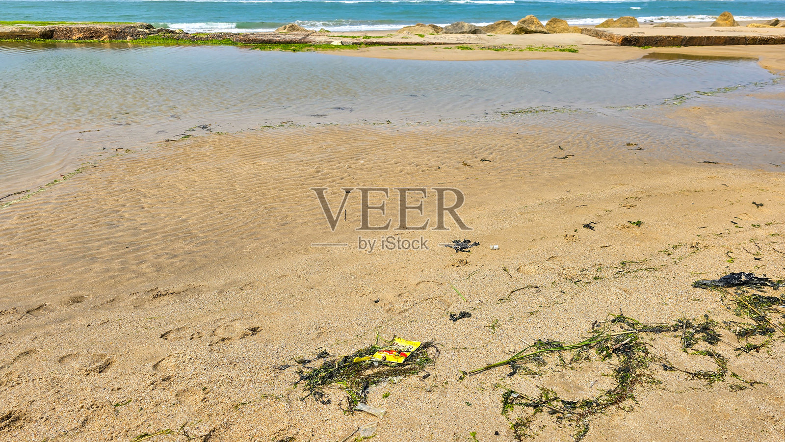 海滩潮湿的沙滩上，有空着的黄色塑料包装和绿色海藻。海洋塑料污染。对环境不负责任的态度。照片摄影图片