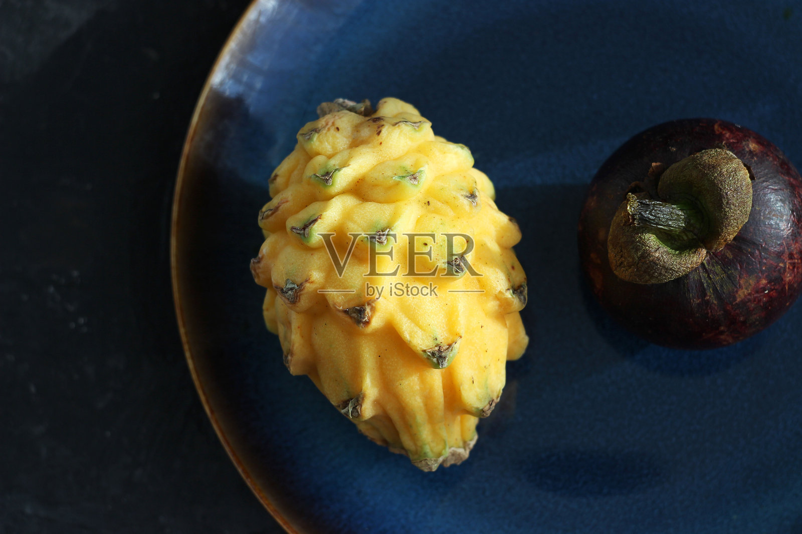 黄色的火龙果和山竹放在桌子上的盘子里照片摄影图片