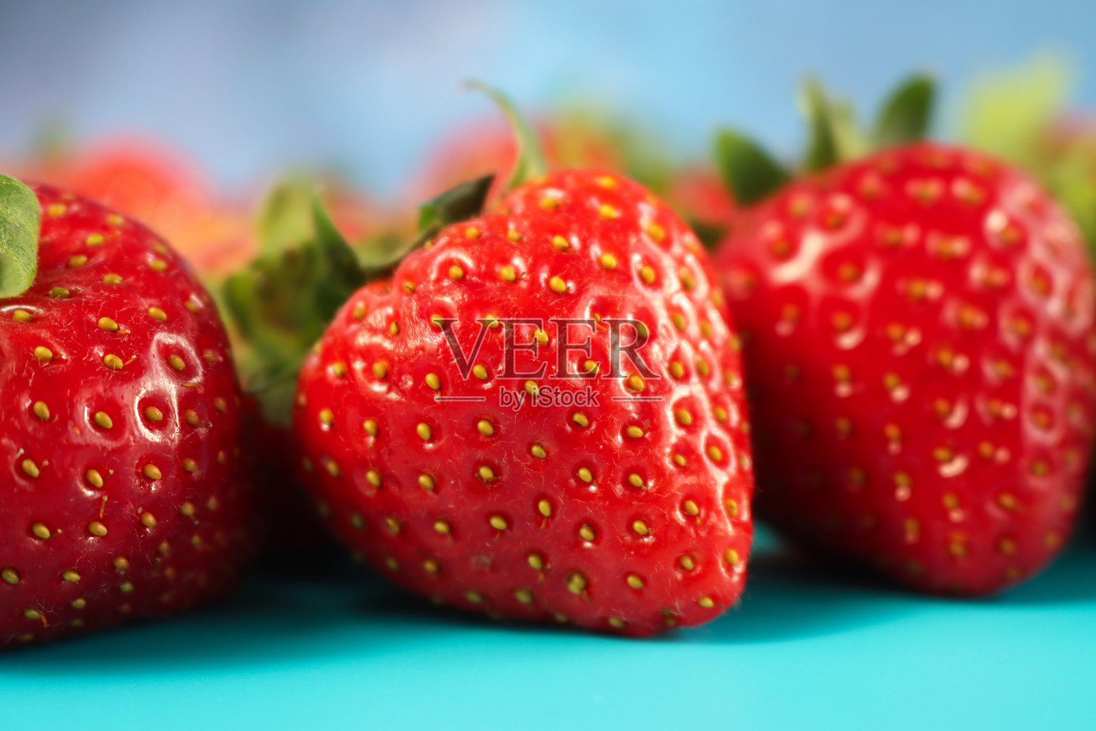 特写镜头，展示了绿叶衬托下的新鲜完整红草莓，背景为青绿色，焦点在前景。照片摄影图片