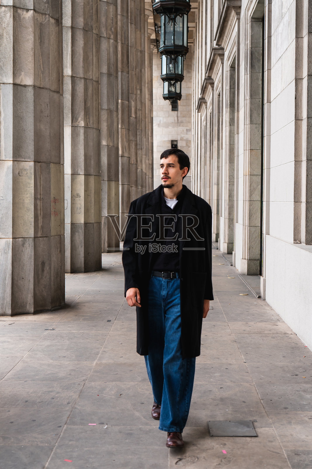 穿着西装的男人沿着带有经典建筑柱子的建筑行走照片摄影图片