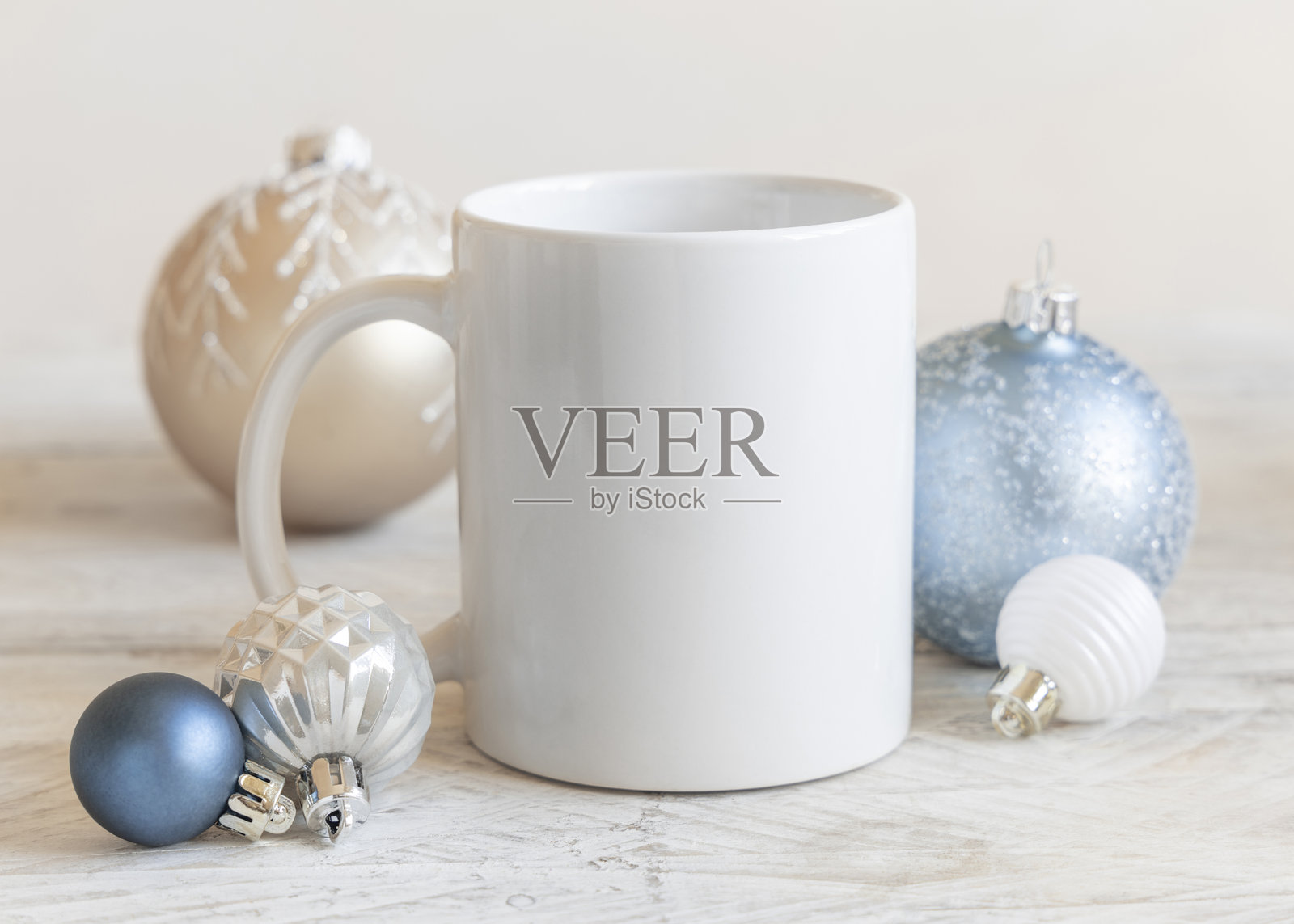 白色空白咖啡杯近景，旁边放着奶油色和浅蓝色的圣诞装饰球，用于模型展示照片摄影图片