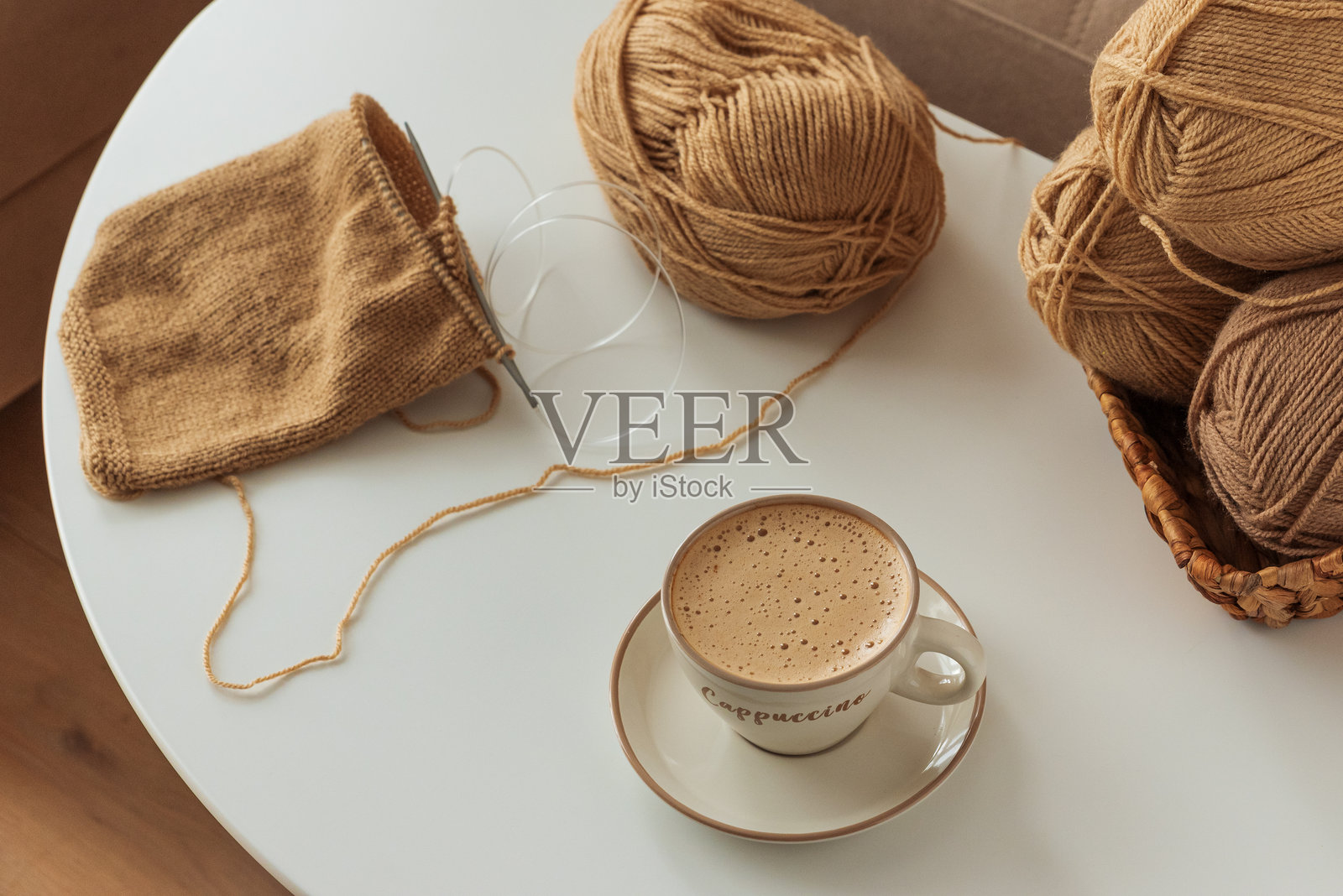 白色桌面上舒适的羊毛编织项目和一杯卡布奇诺咖啡照片摄影图片