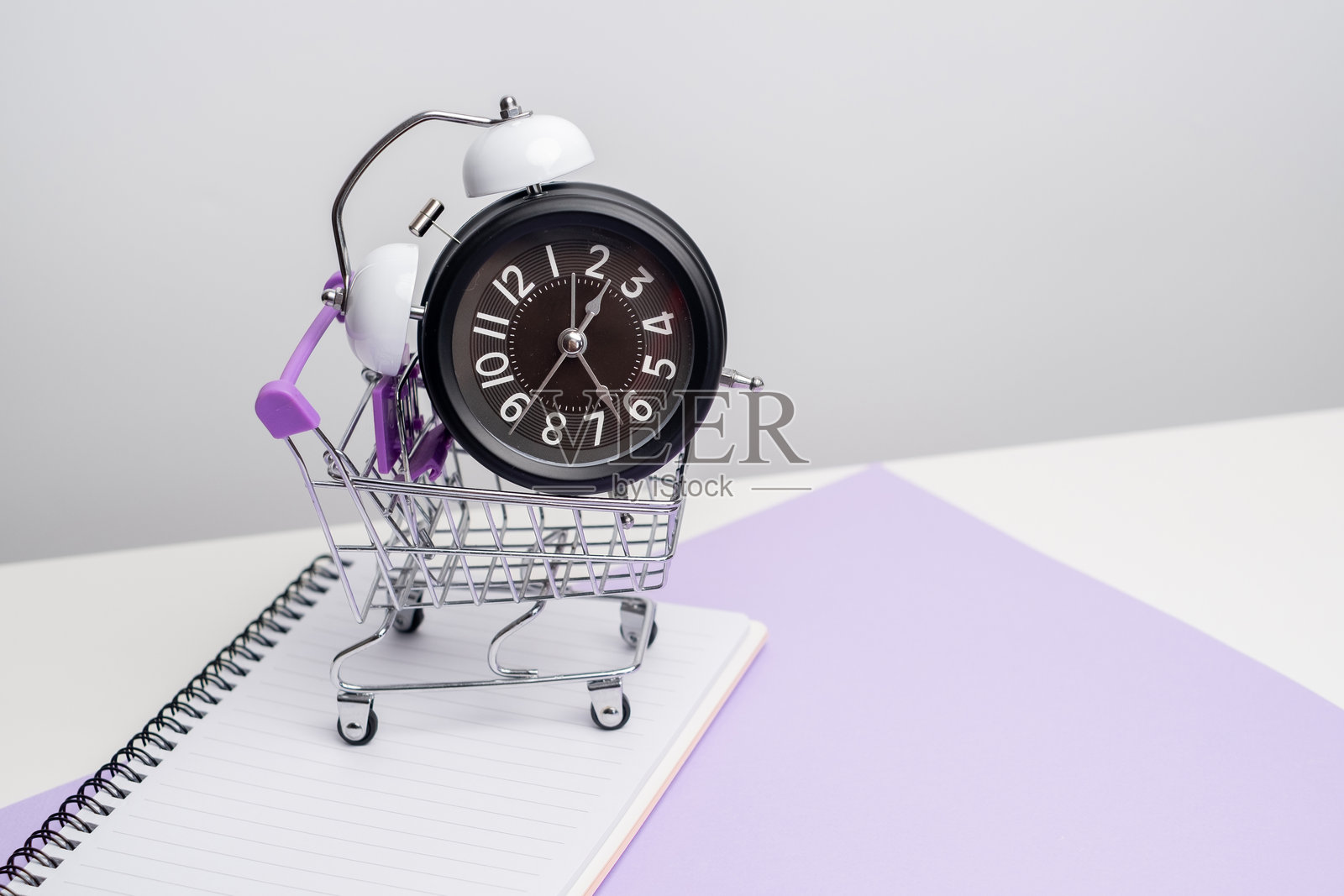 时间管理概念。笔记本上的购物车里放着闹钟，极简构图，背景为浅色。照片摄影图片