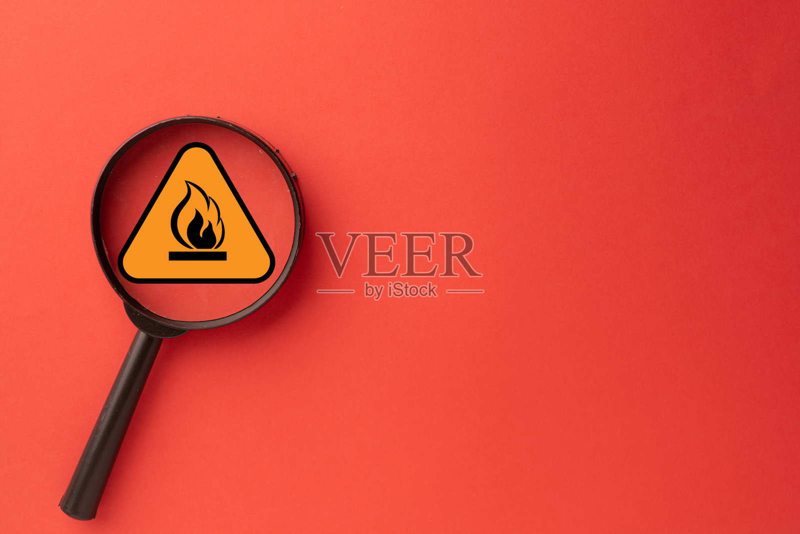 聚焦火灾隐患：放大镜置于红色背景上的易燃警告标志上方照片摄影图片