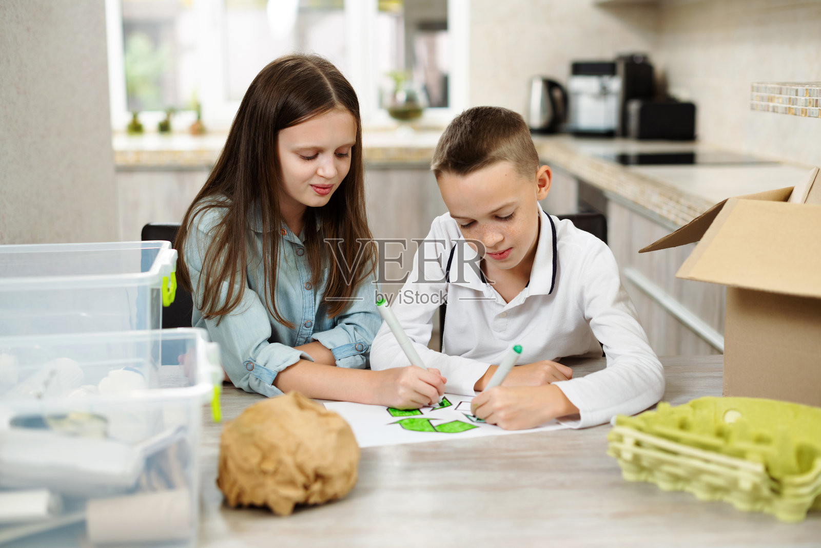 孩子们在家里的厨房里画回收符号。孩子们在家里的厨房里将纸张和塑料分类到分类箱中。垃圾分类、垃圾分类、垃圾回收。照片摄影图片