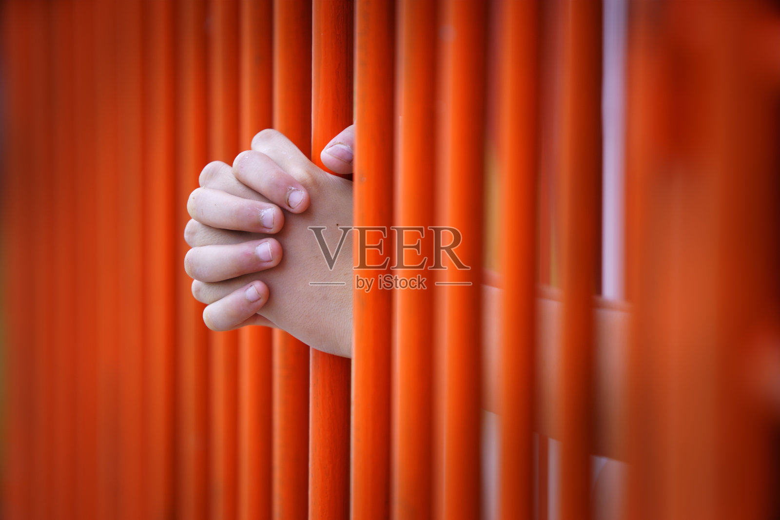 双手紧握明亮的橙色栅栏，背景模糊照片摄影图片