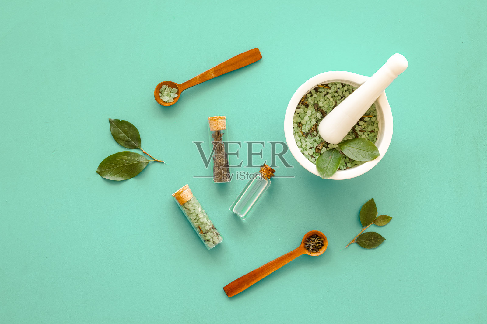 自制有机化妆品 - 研钵中盛有茶树精油和海盐，旁边有绿叶，背景为绿色，俯视角度照片摄影图片