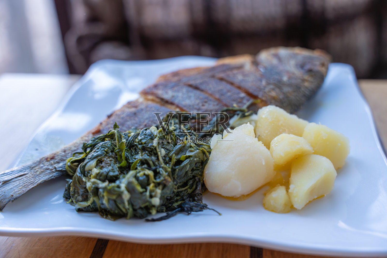 白盘烤全鱼配菠菜和土豆。照片摄影图片