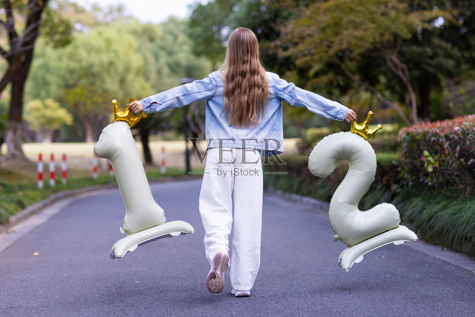 年轻女孩在公园户外散步，手里拿着数字气球照片摄影图片