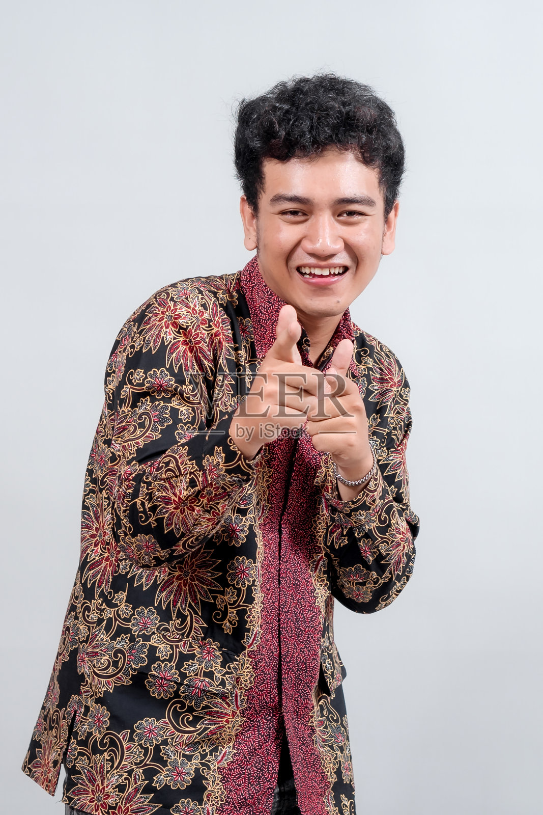 一个年轻男子身穿色彩鲜艳的蜡染衬衫，伸出大拇指，笑容灿烂，自信而快乐地摆出姿势，背景简洁。照片摄影图片