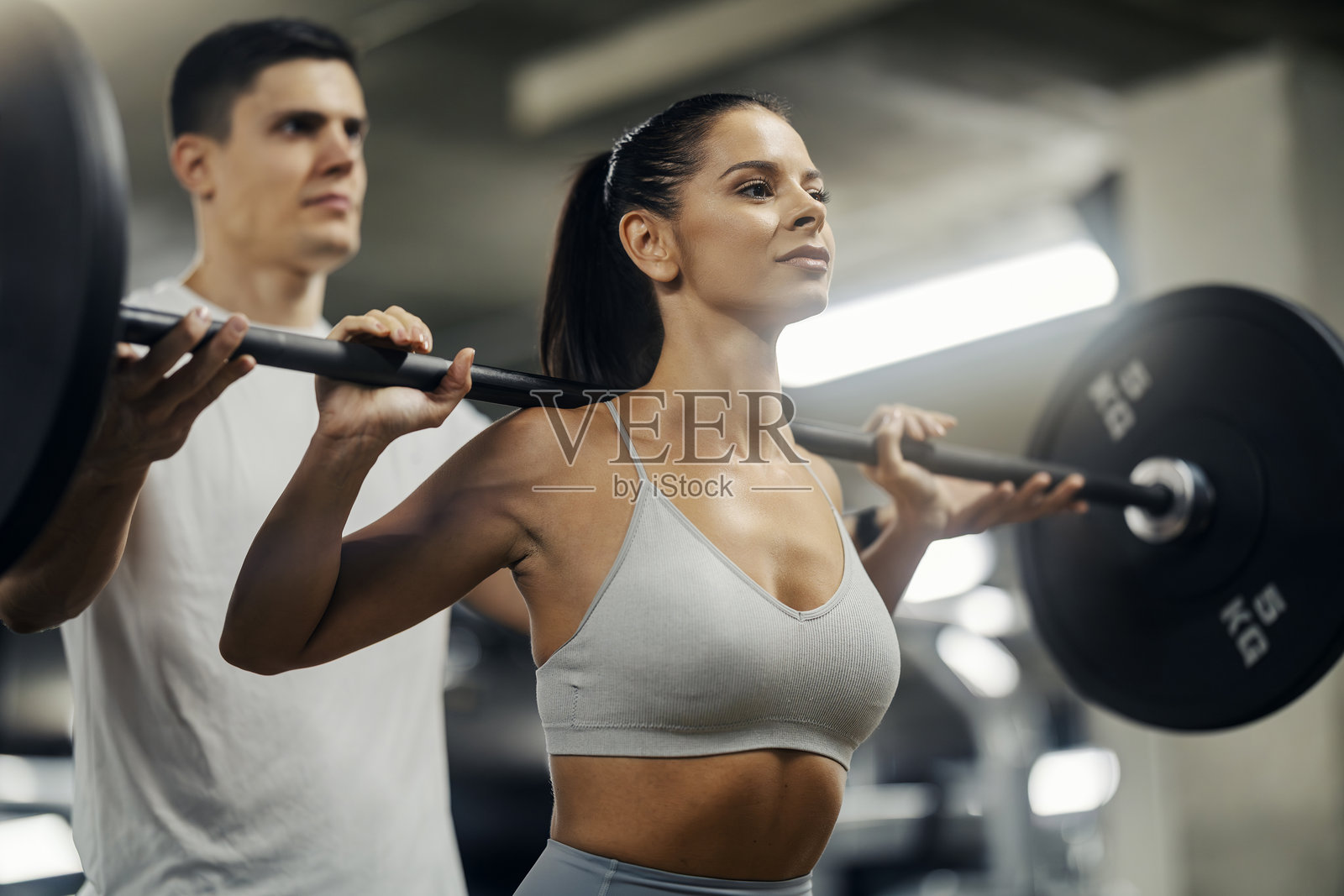 女子在健身房举重，旁边有私人教练指导照片摄影图片