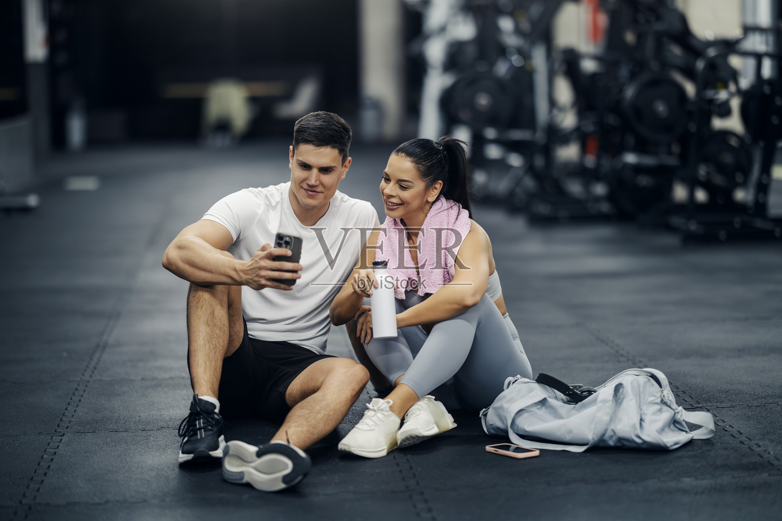 情侣在健身房锻炼后使用智能手机休息照片摄影图片