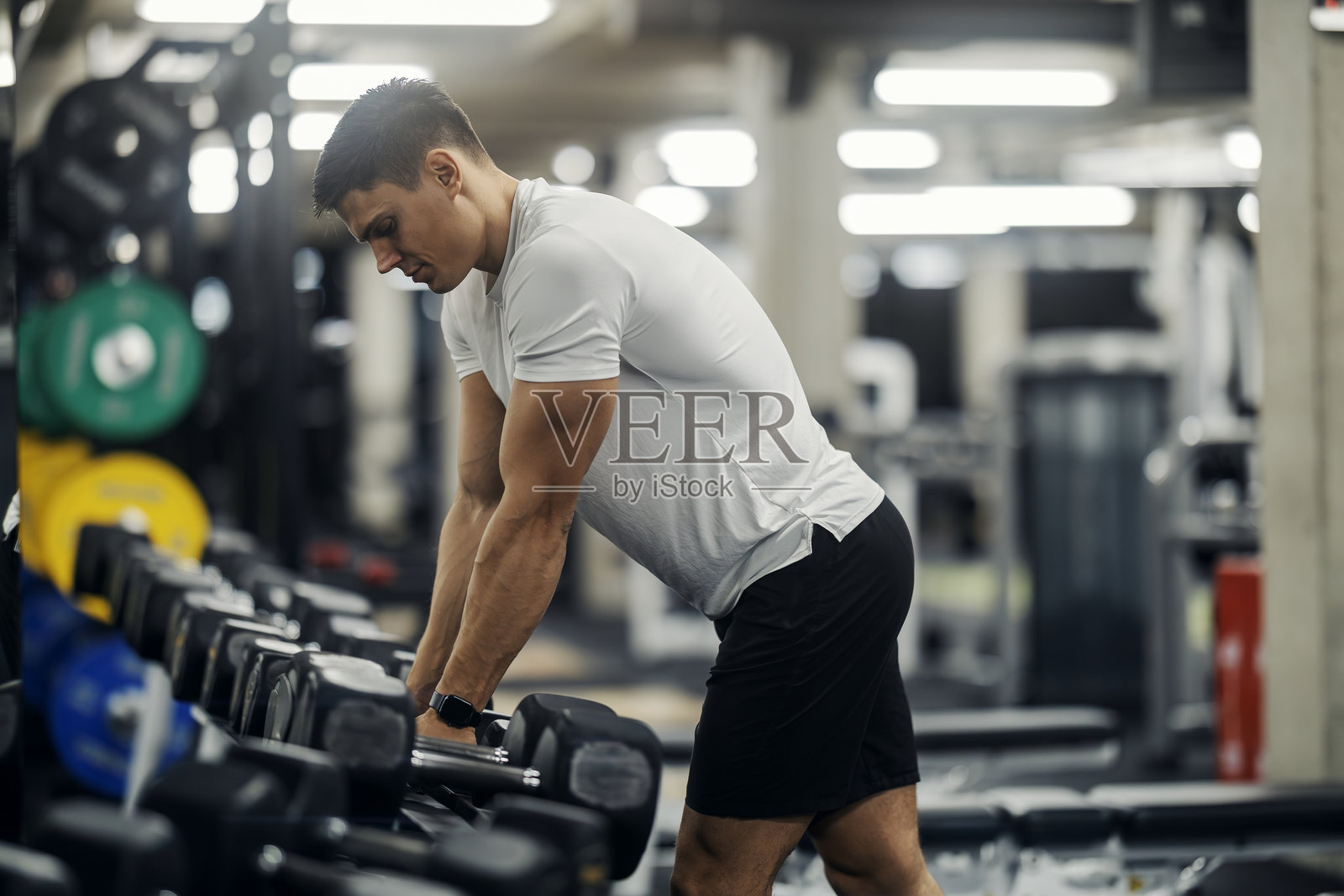 年轻男子在健身房锻炼时选择哑铃照片摄影图片