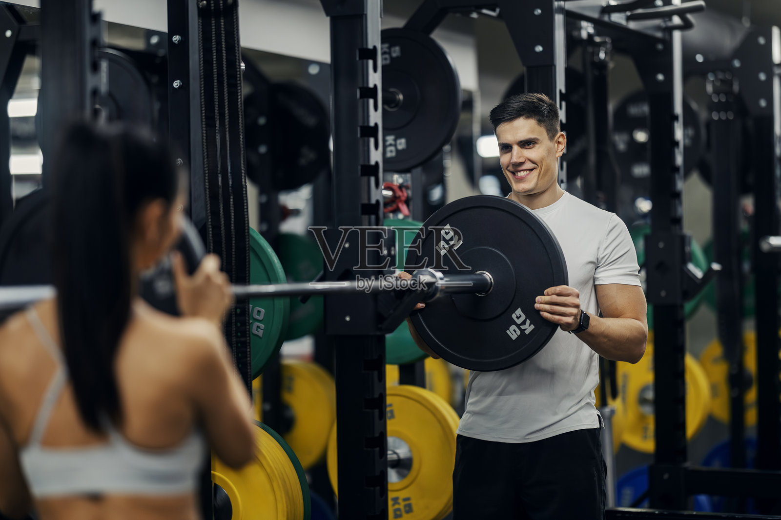 男人在健身房帮忙女人给杠铃增加重量照片摄影图片