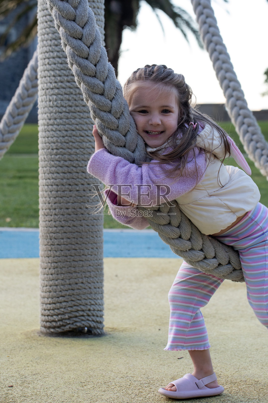 一个快乐的小女孩在户外游乐场玩耍，爬着秋千绳。童年照片摄影图片