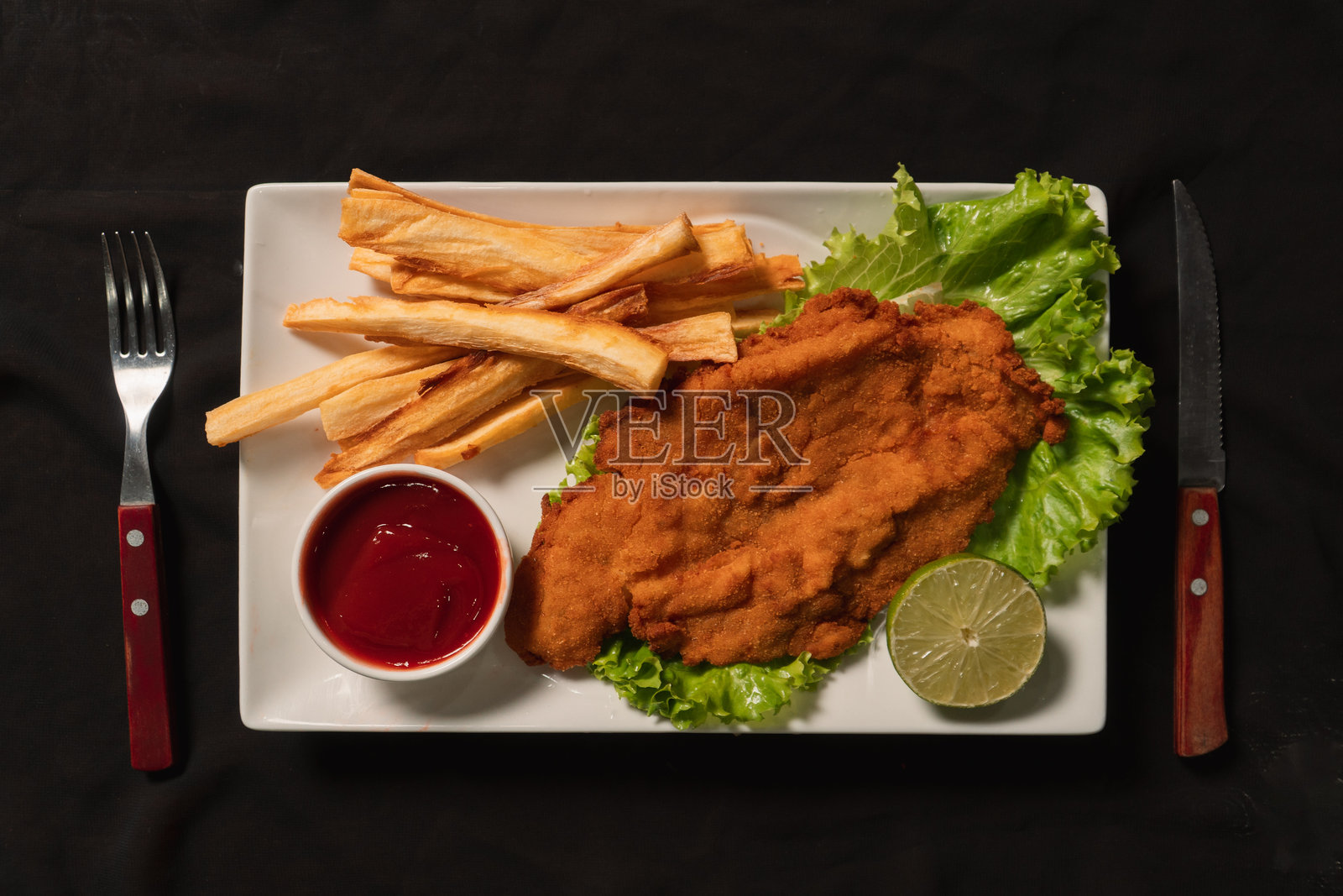 白盘子里的炸肉排配炸薯条和番茄酱，配有餐具的俯视图。照片摄影图片