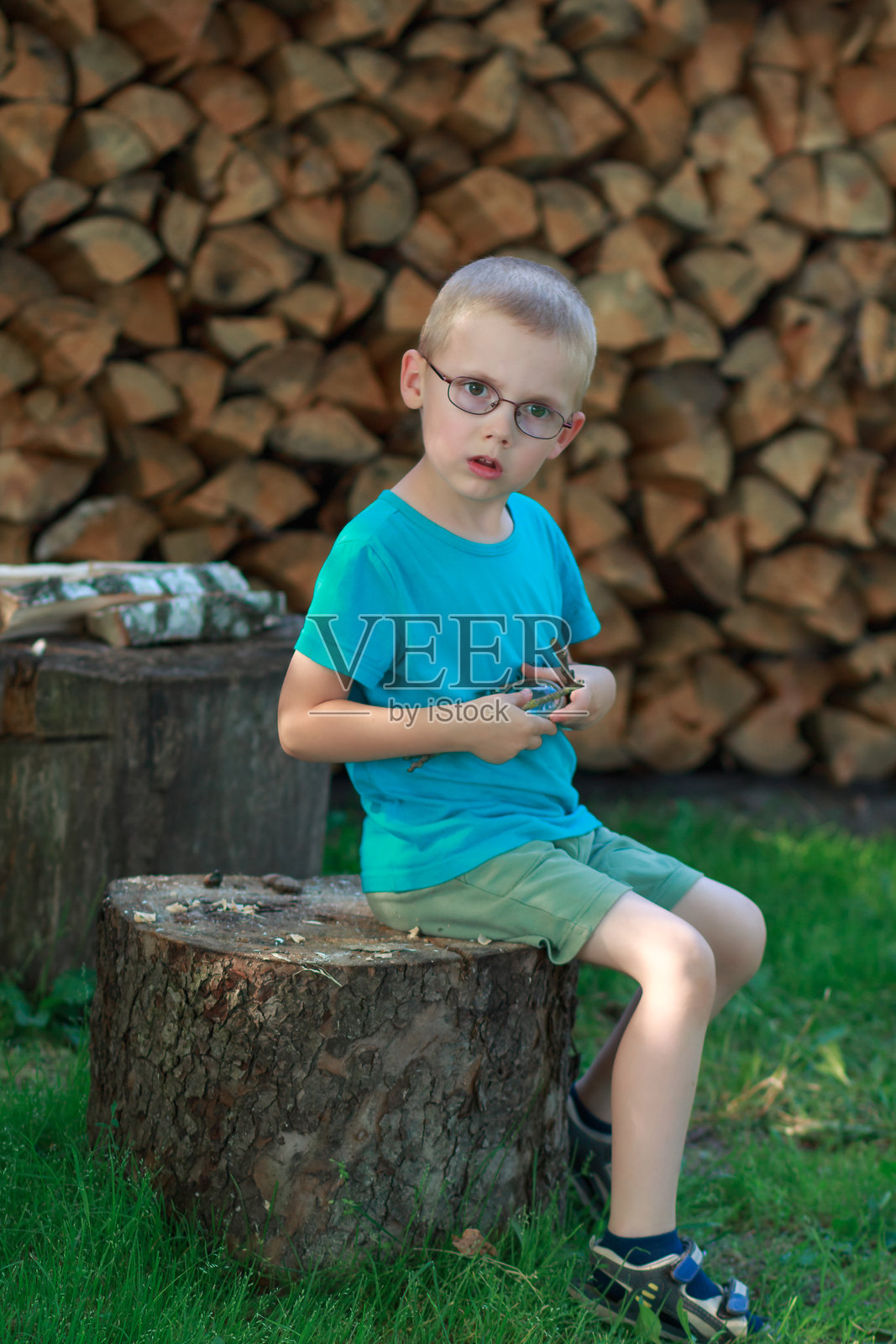一个男孩坐在木桩上，背景是柴火。照片摄影图片