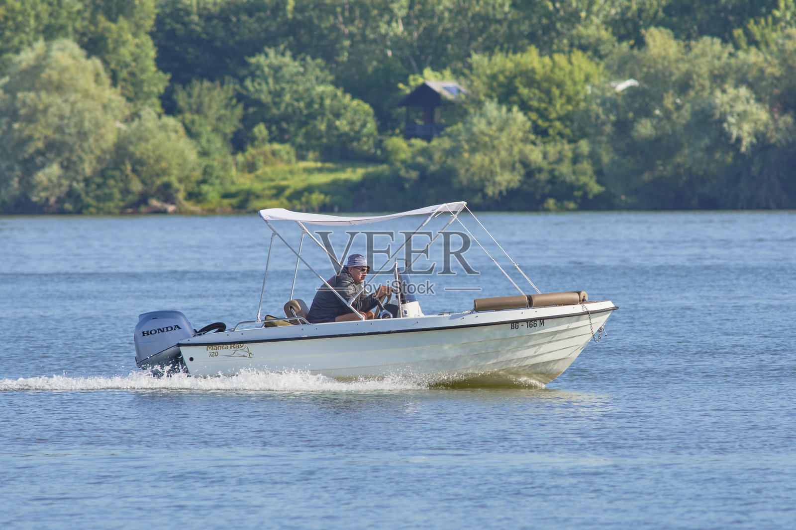 塞尔维亚贝尔格莱德，一个男人在多瑙河上驾驶着一艘小型摩托艇，背景是郁郁葱葱的绿植。照片摄影图片
