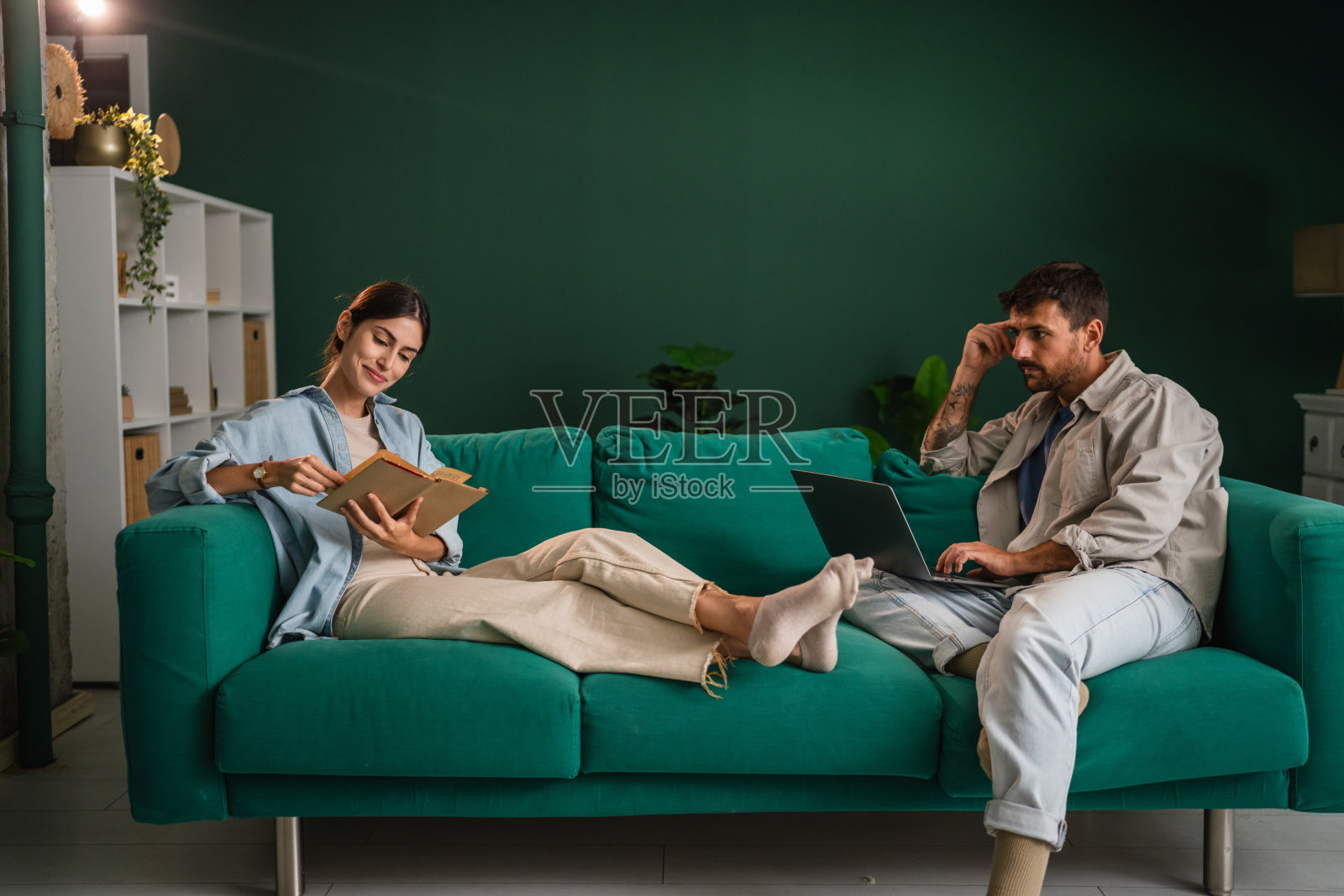 情侣在沙发上放松，一人看书，一人使用笔记本电脑照片摄影图片