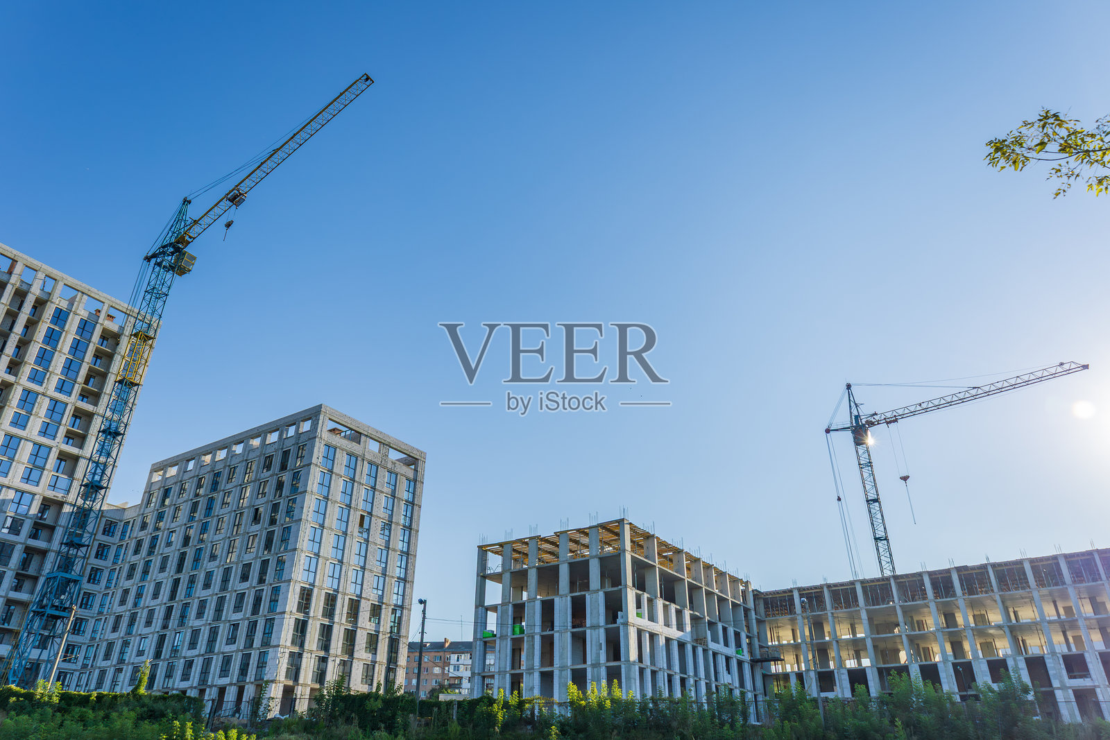 建筑工人在建筑工地上积极地建造新的住宅建筑，上方有起重机和明亮的蓝天。照片摄影图片