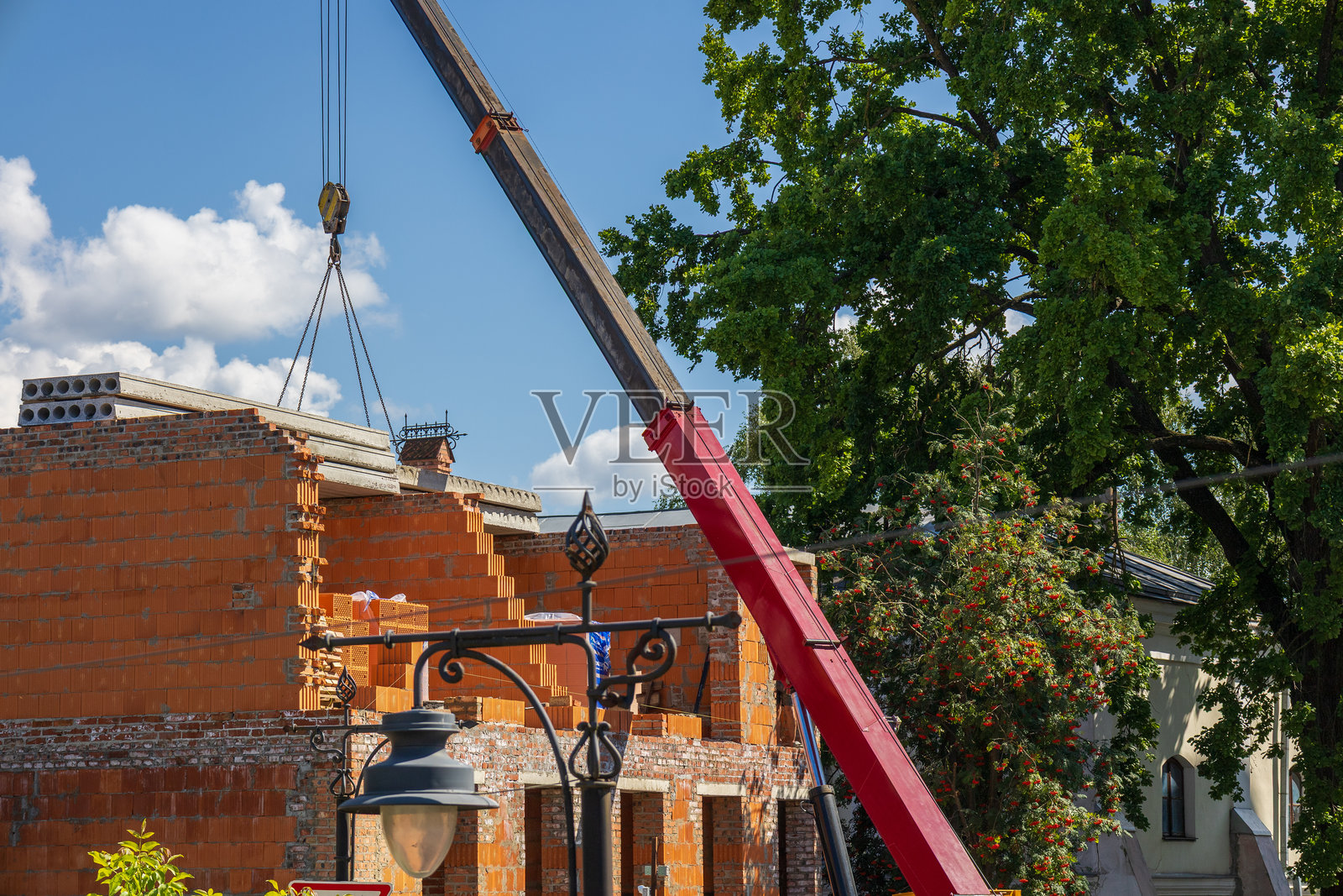 晴天时，起重机正在居民区一栋未完工的房子上吊装建筑材料照片摄影图片