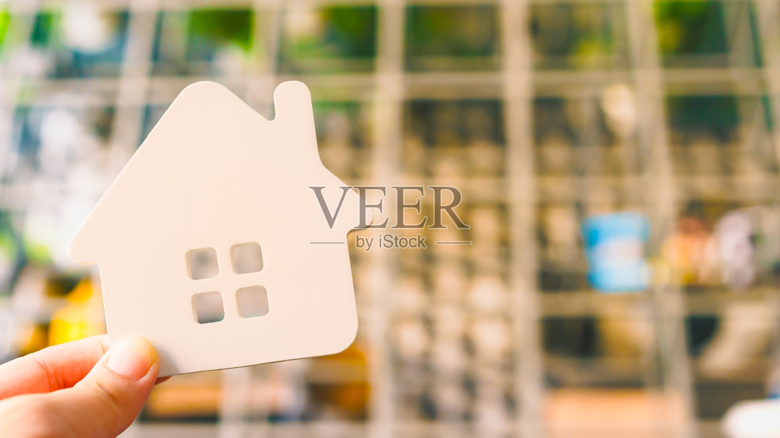 手持带有窗户镂空的白色房屋模型，象征着房地产、房屋所有权、住房市场、抵押贷款或物业投资。代表着购买、租赁或梦想家园的概念。照片摄影图片